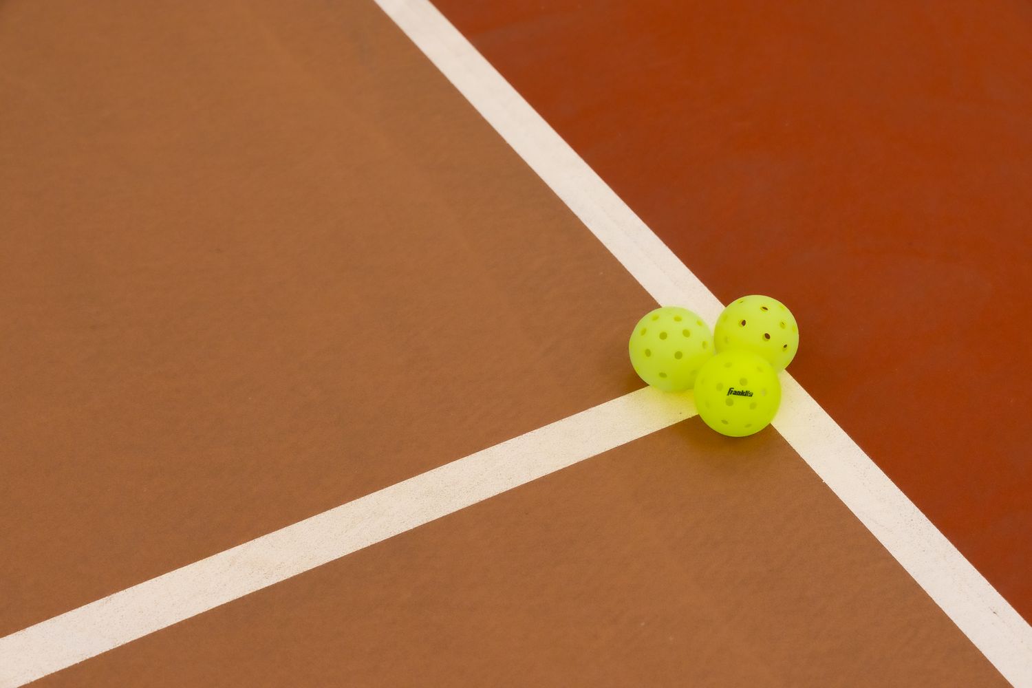 Three yellow pickleballs resting on a brown court near white boundary lines.