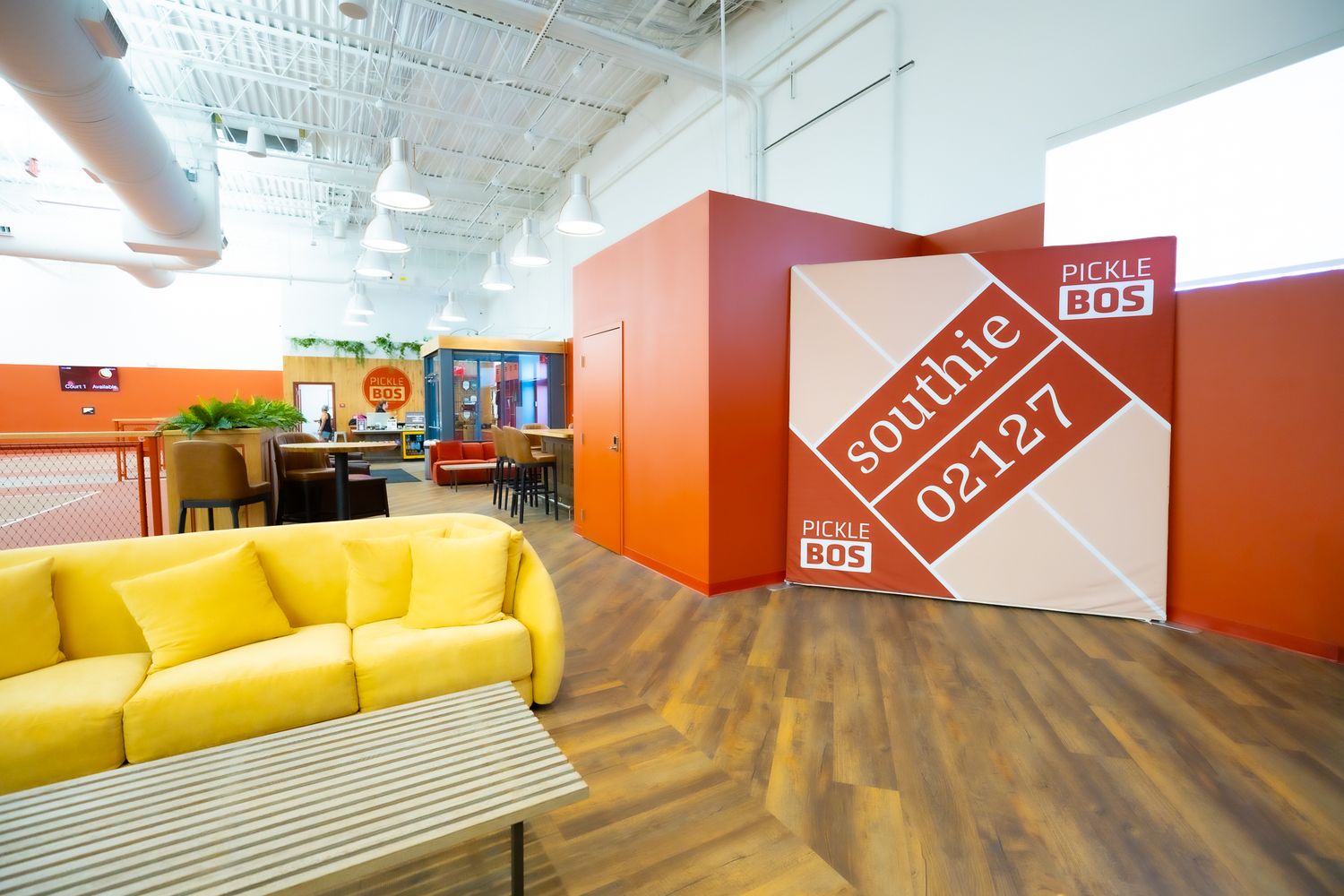 Modern coworking space with yellow sofa, orange accent wall, and Southie BOS 02127 signage on hardwood floors.