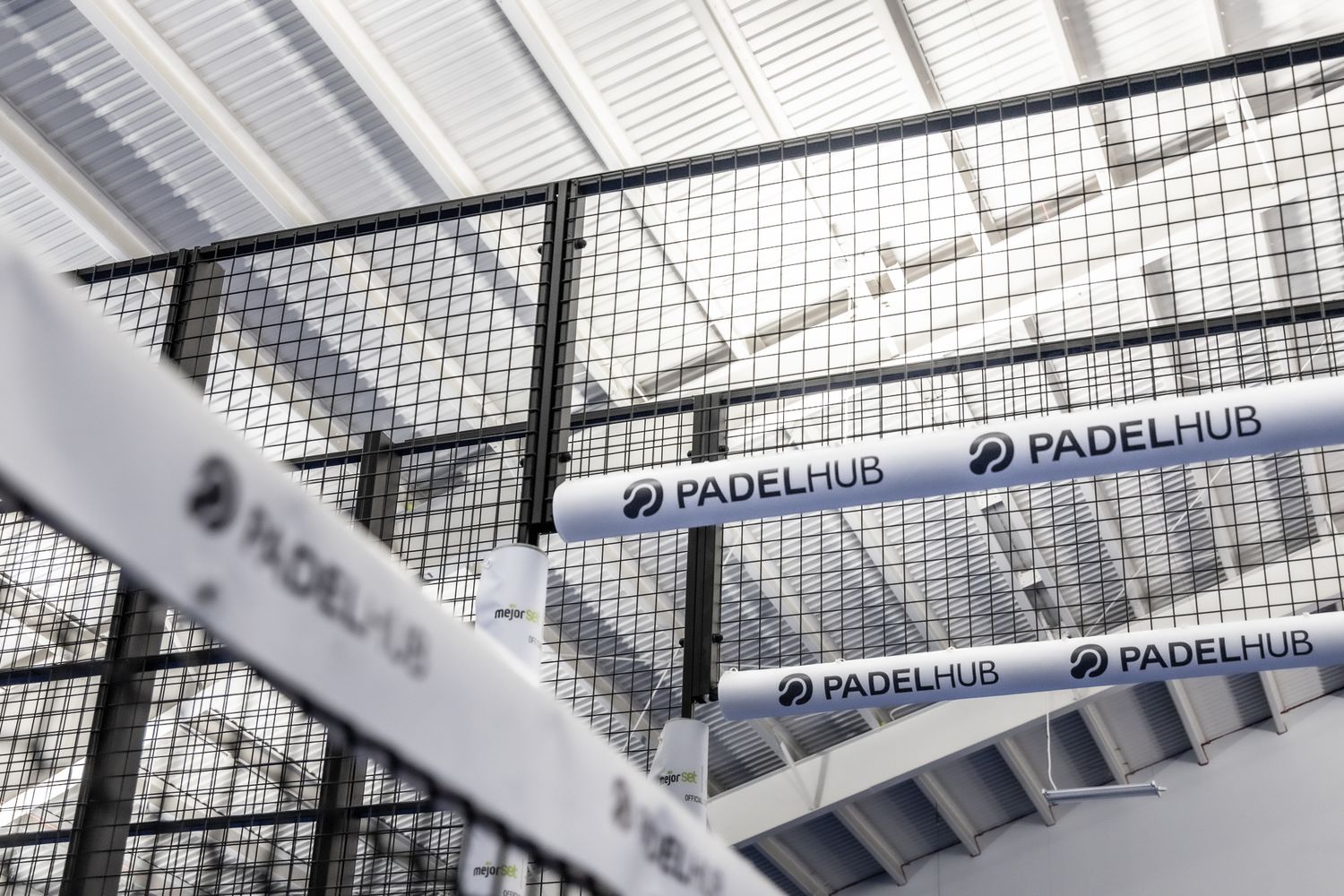 PadelHub branded banners displayed on metal fencing structure inside indoor padel facility.