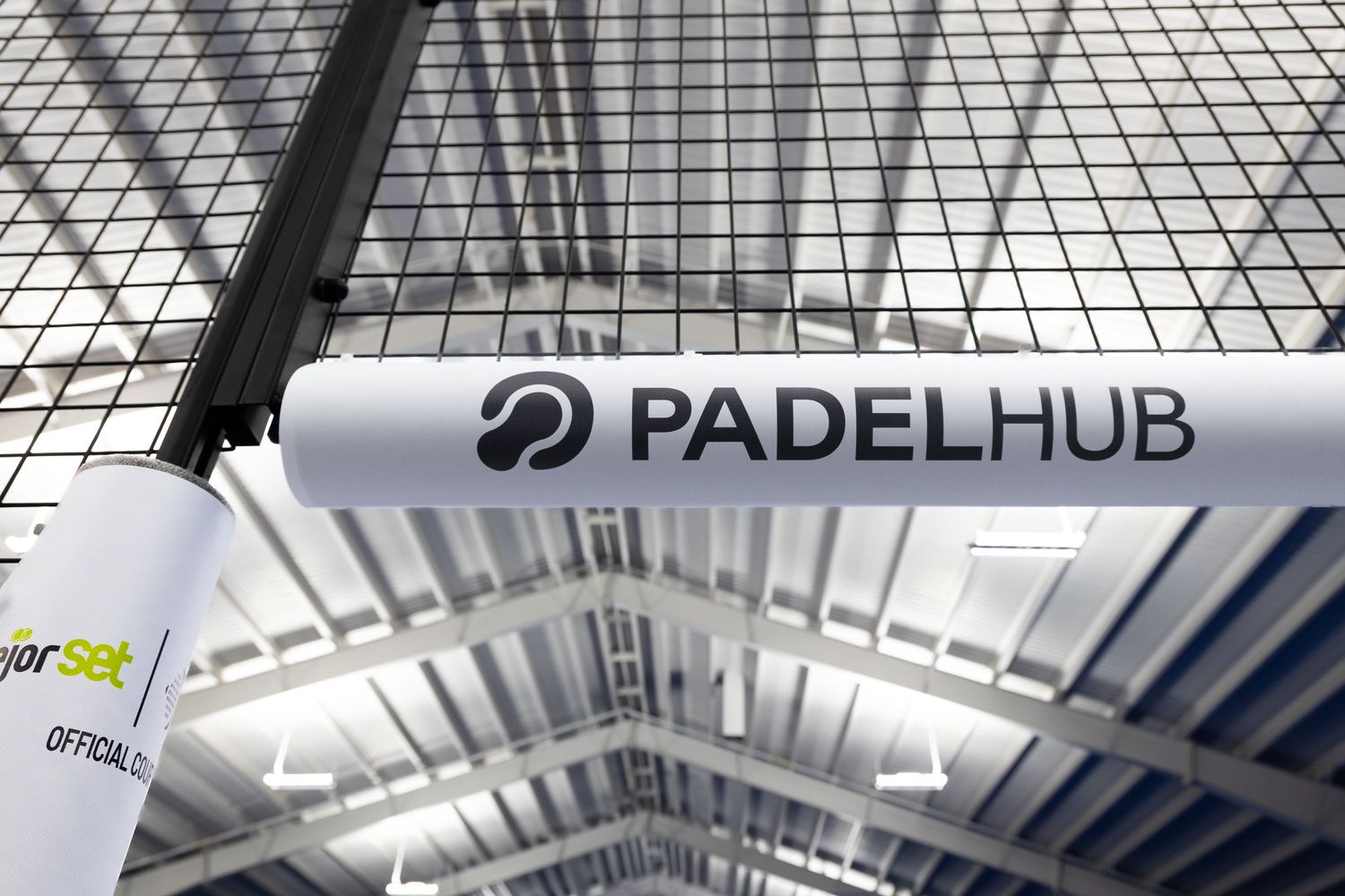 PadelHub logo displayed on a curved overhead banner inside an indoor padel sports facility.