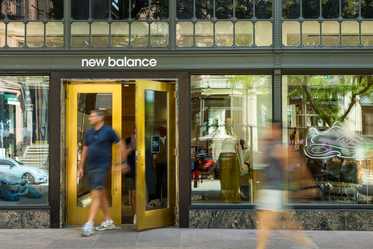 New balance retail store front with gold doors and pedestrians walking by on a city street.