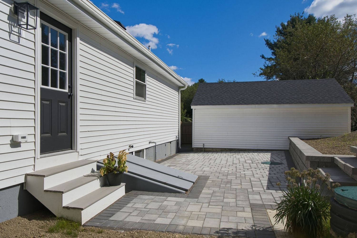 Paver patio with steps and ramp leading to white vinyl sided home with detached garage in background.