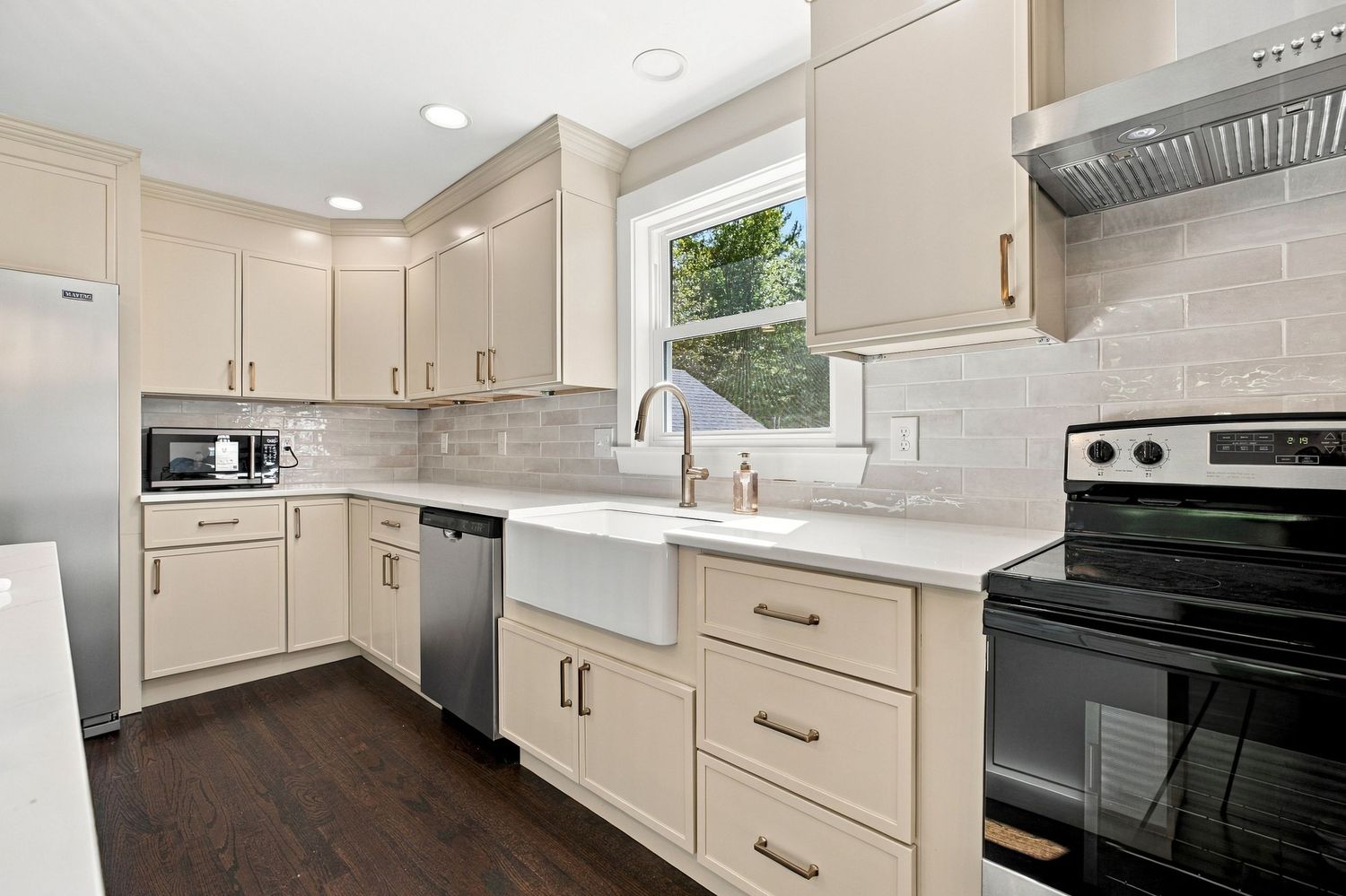Modern kitchen with cream cabinets, farmhouse sink, subway tile backsplash, stainless appliances, and dark hardwood floors.