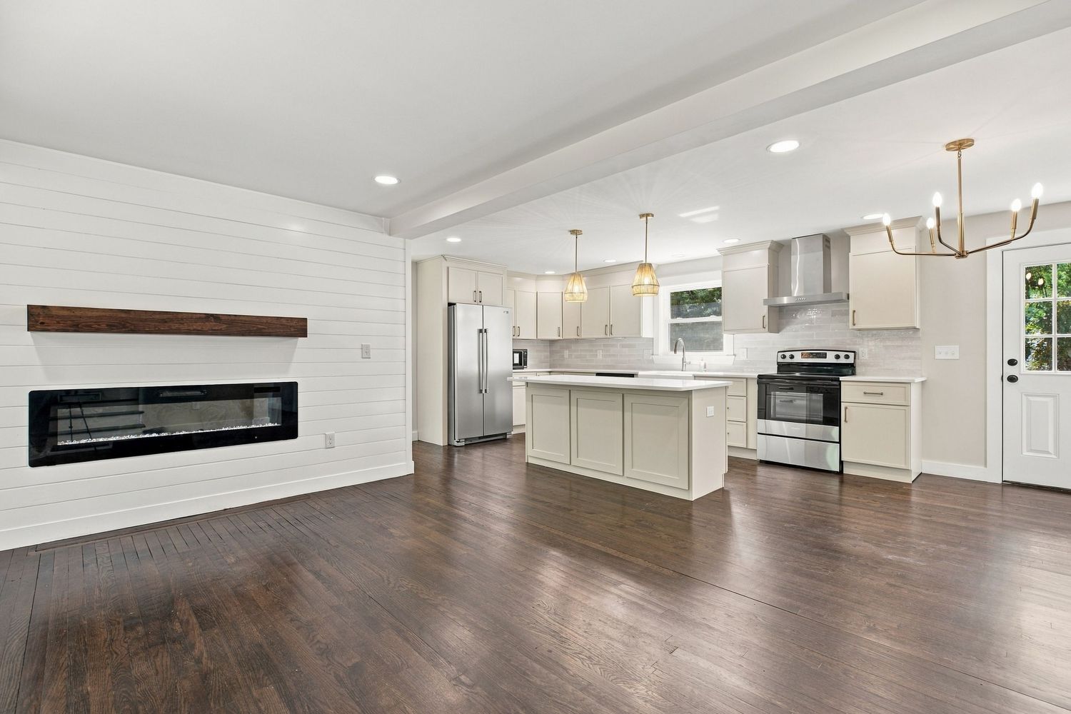 Open-concept kitchen with white cabinets, island, stainless appliances, hardwood floors, and modern fireplace in living area.