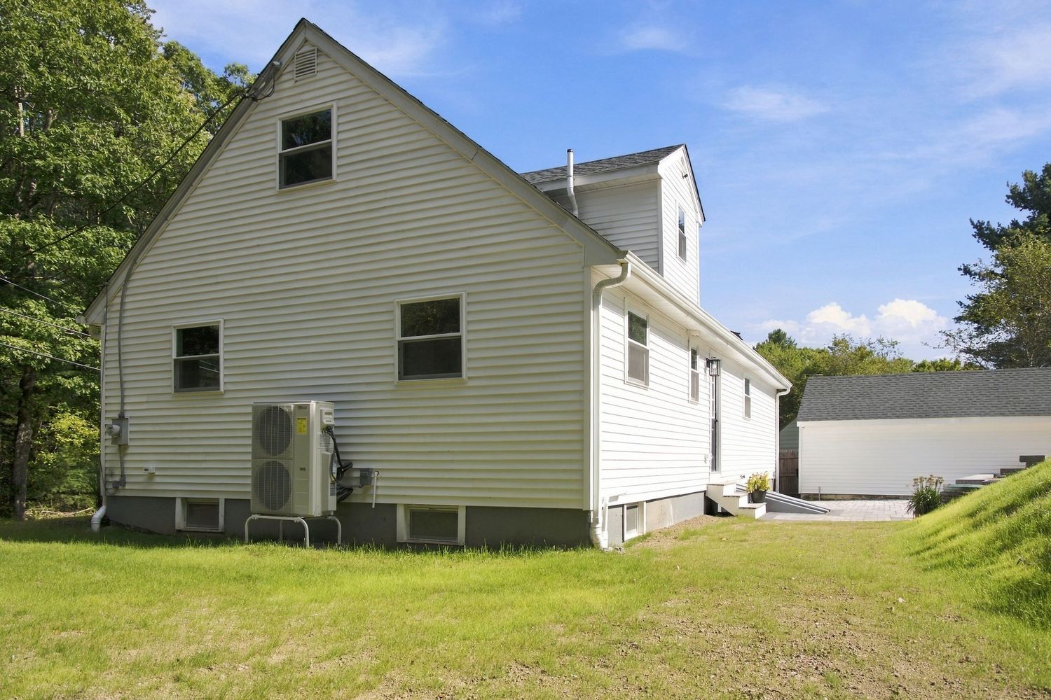 Rear exterior view of a white two-story home with HVAC unit, green lawn, and surrounding trees on a sunny day.