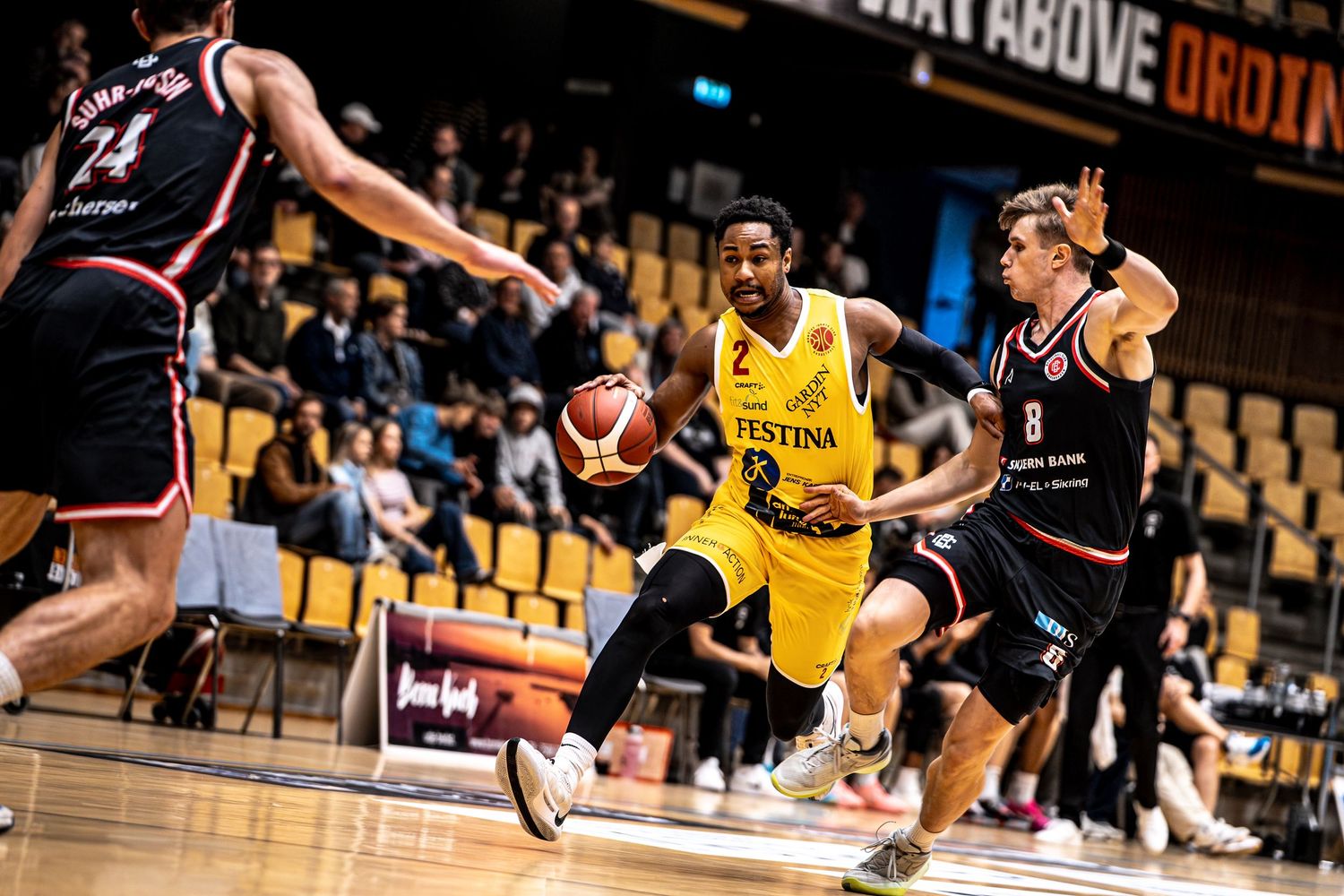 Basketball player number 2 in yellow jersey dribbles past defender during competitive league game.
