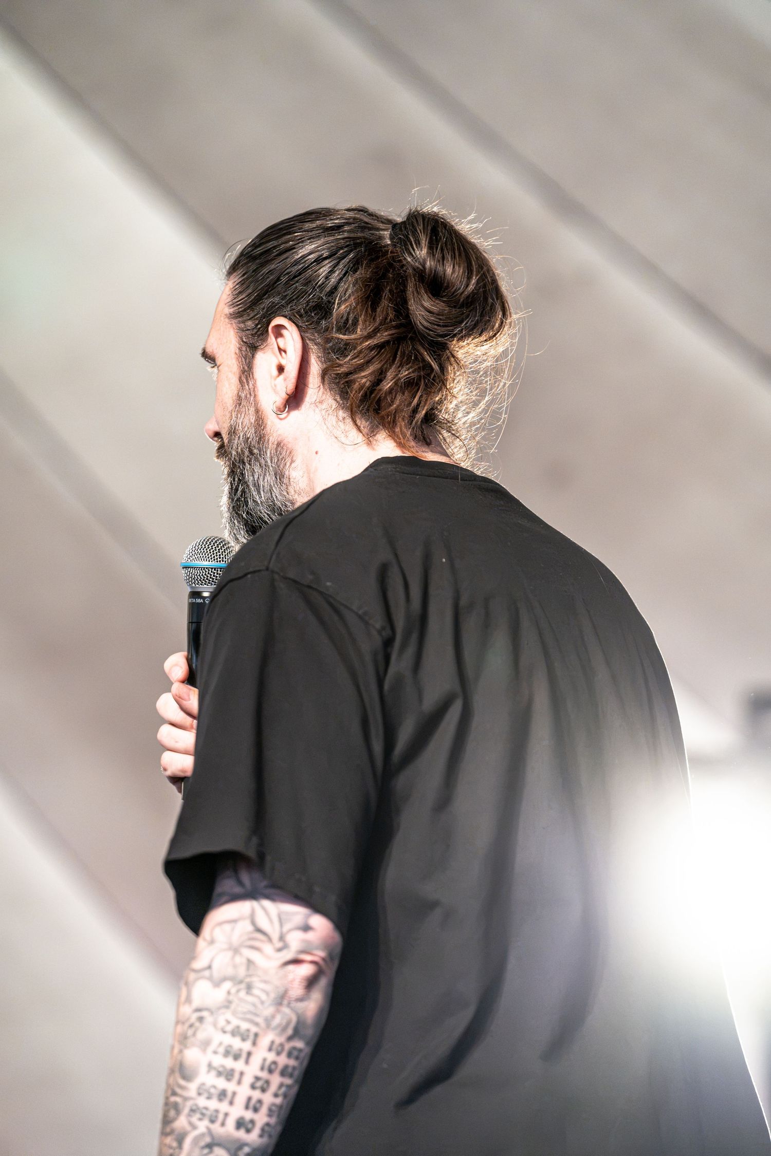 Close-up of bearded tattooed male singer holding microphone with hair in bun at live concert.