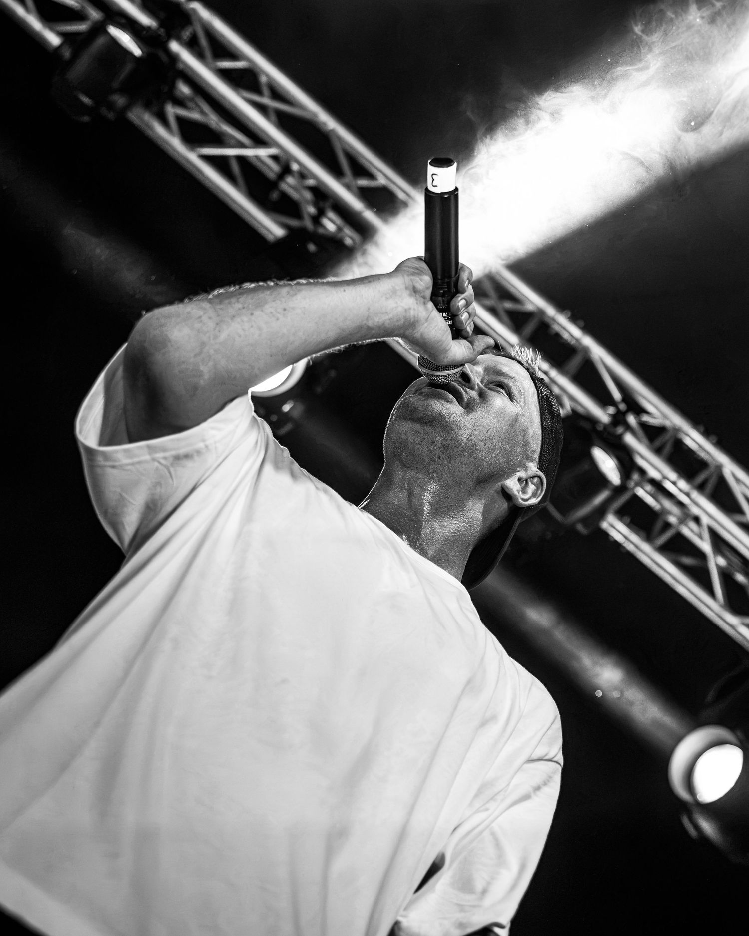 Black and white shot of male vocalist singing intensely into microphone on stage.