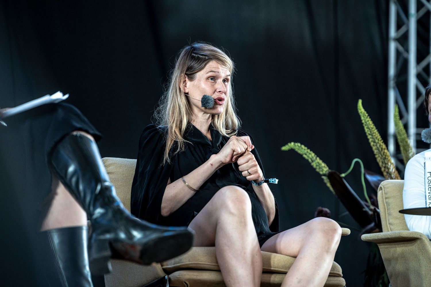 Woman in black dress speaking into microphone on stage at outdoor event.