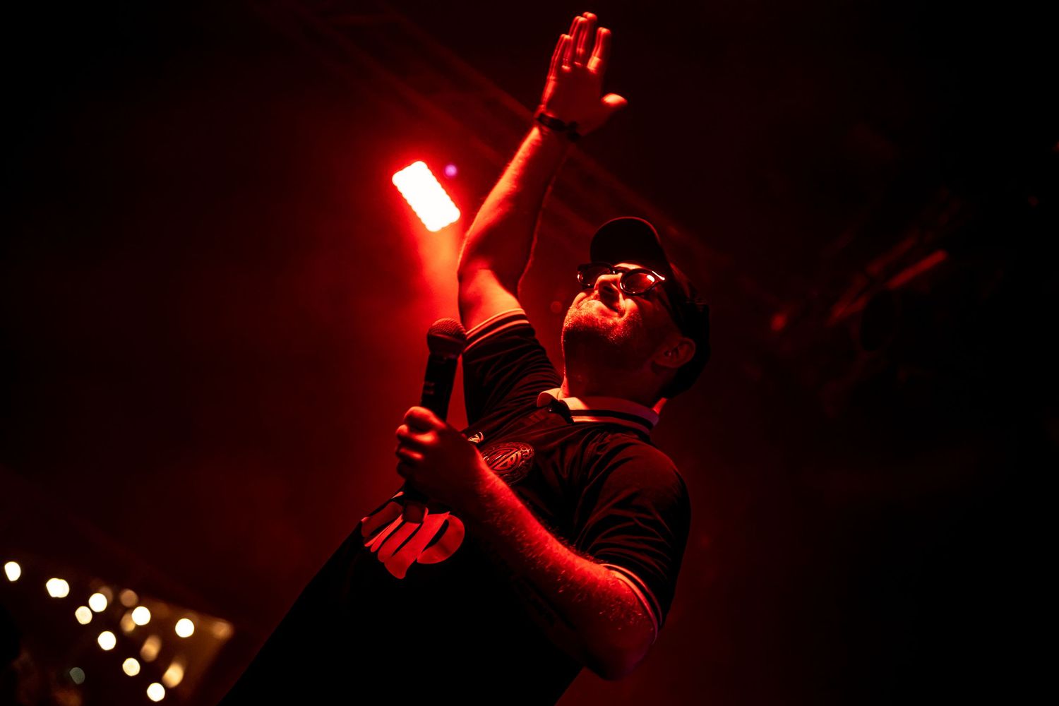 Performer raises hand toward red stage light during energetic live concert performance.