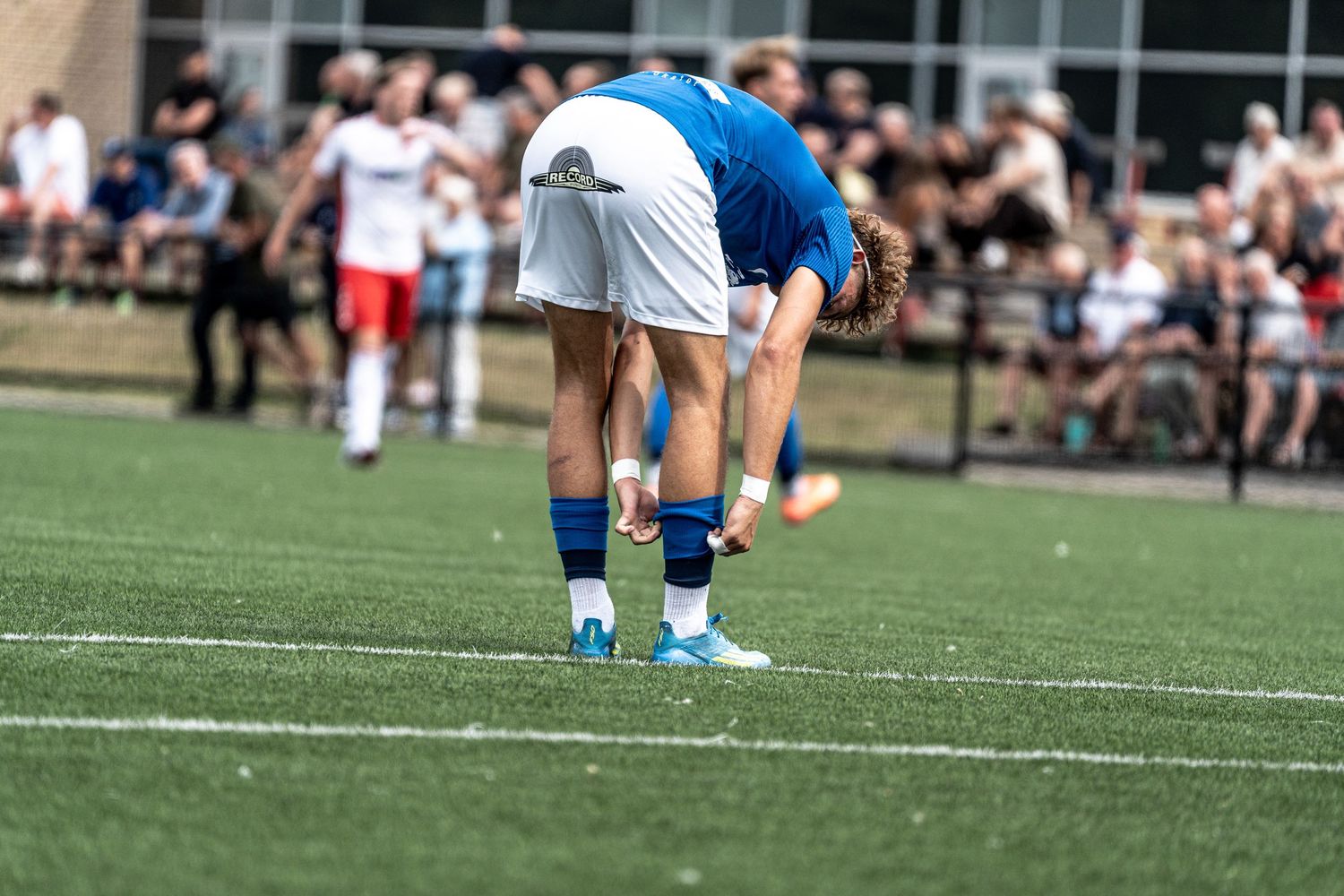 Soccer player in blue and white uniform bending down on green turf field during outdoor match.