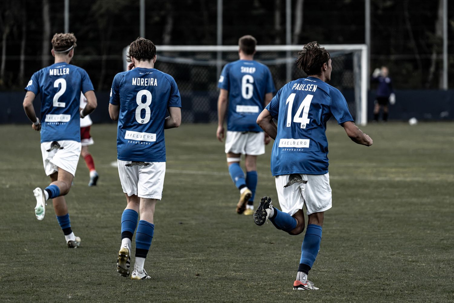 Four soccer players in blue and white uniforms walk on field during a match.