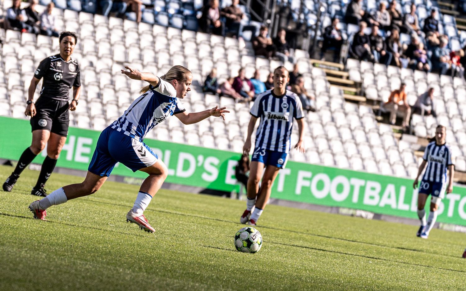 Female footballer in blue-white strip prepares to shoot during a women's soccer match at a stadium.