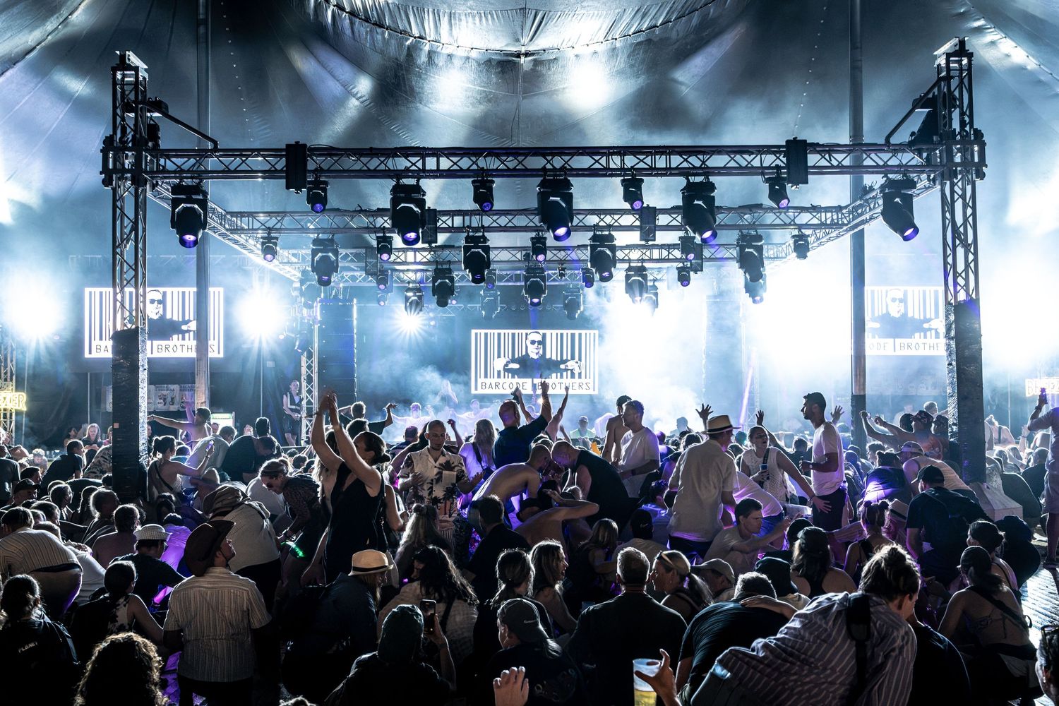 Large crowd enjoys live music under dramatic stage lighting at indoor festival venue.