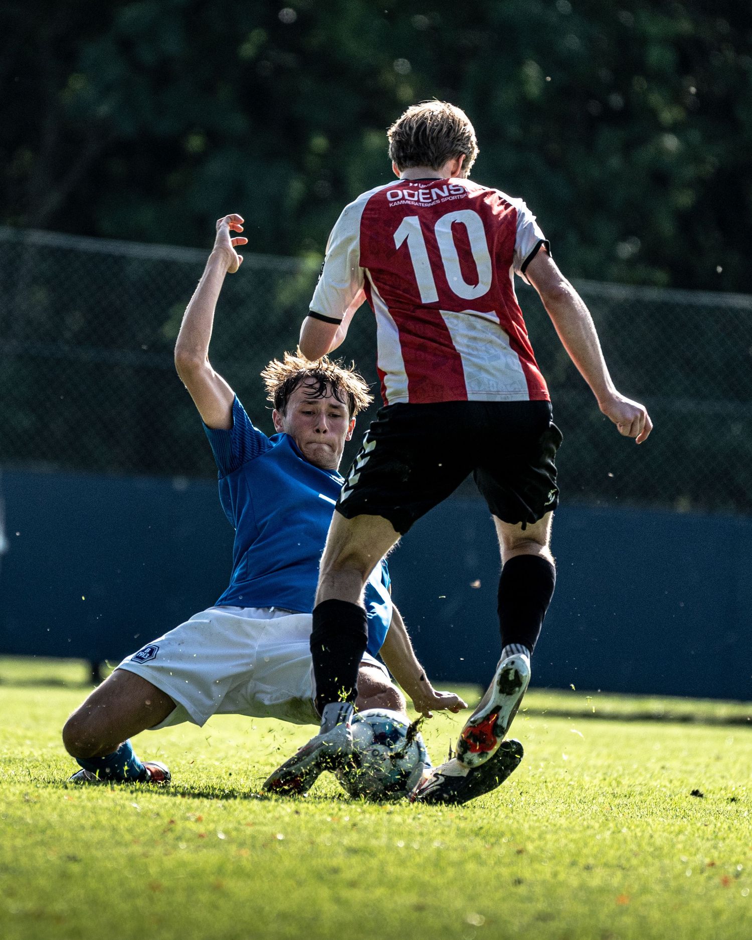 Sliding tackle by blue-kitted player against opponent number 10 in red and white jersey.