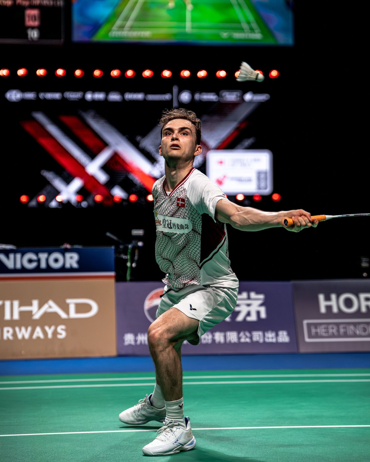Male badminton player looking up tracking shuttlecock during VICTOR sponsored indoor badminton championship.