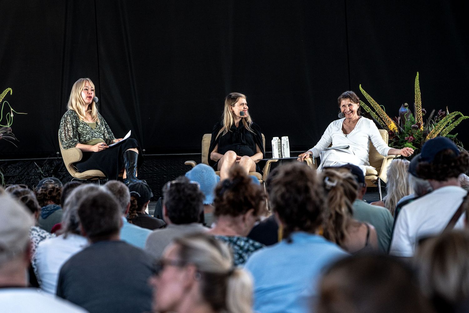 Three panelists speaking to large audience at outdoor stage event.