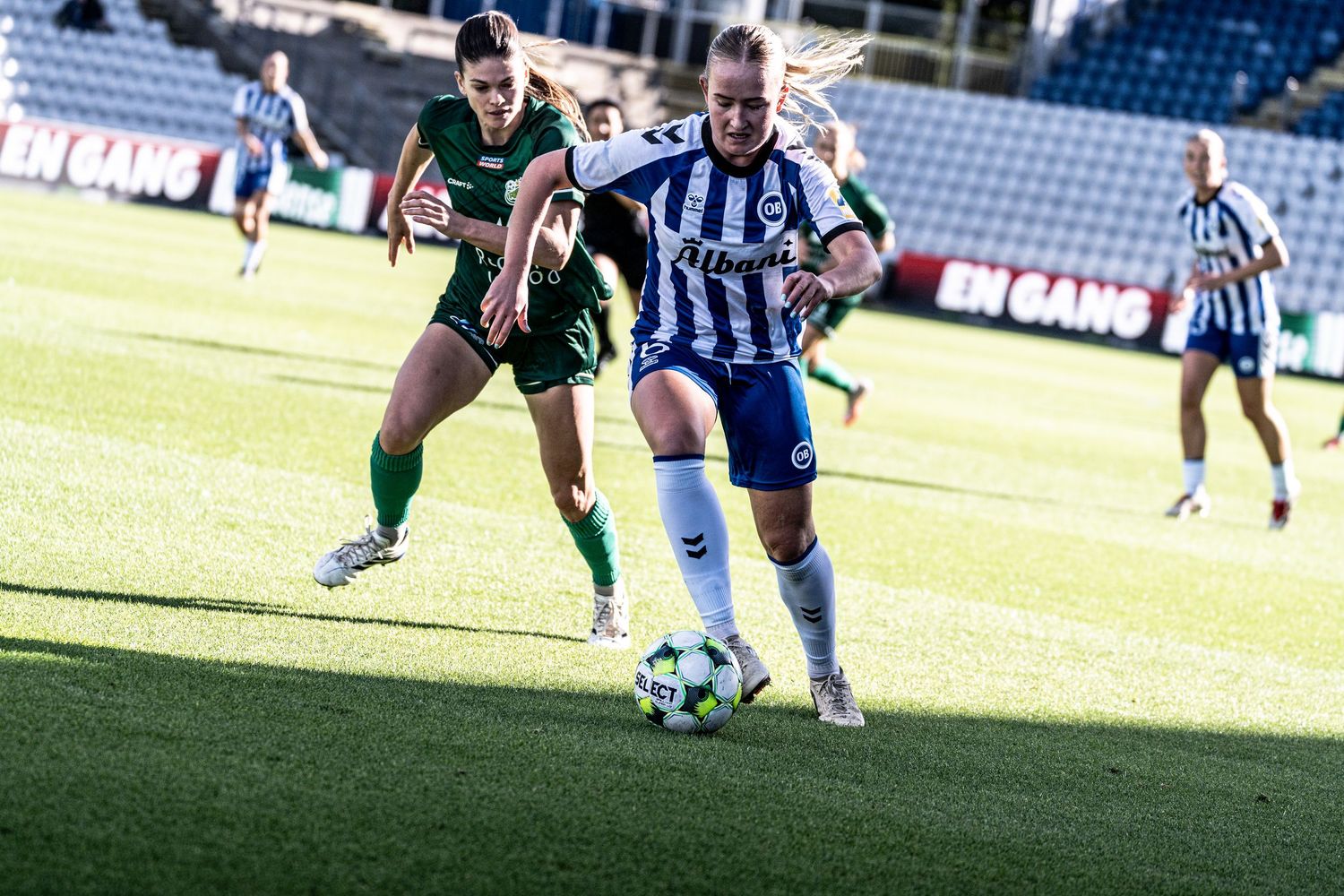 Female footballer in blue and white Albani kit dribbling ball during outdoor match.