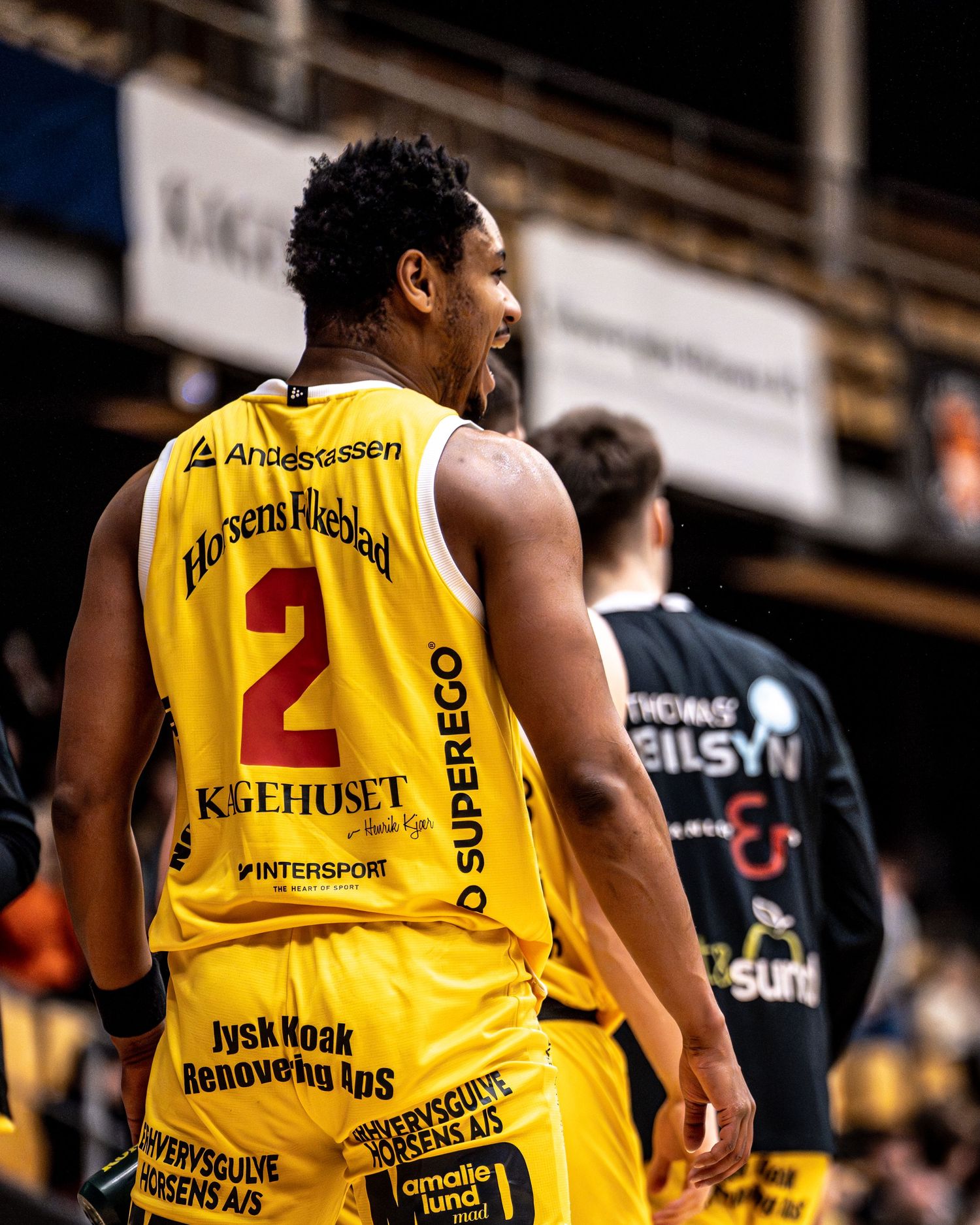 Basketball player number 2 in yellow jersey with sponsors walks on court during game.