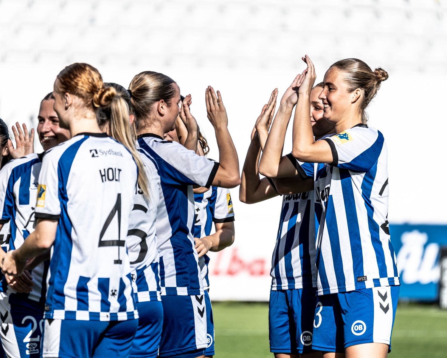 OB women's soccer team celebrates goal with high-fives on the pitch during a home match.
