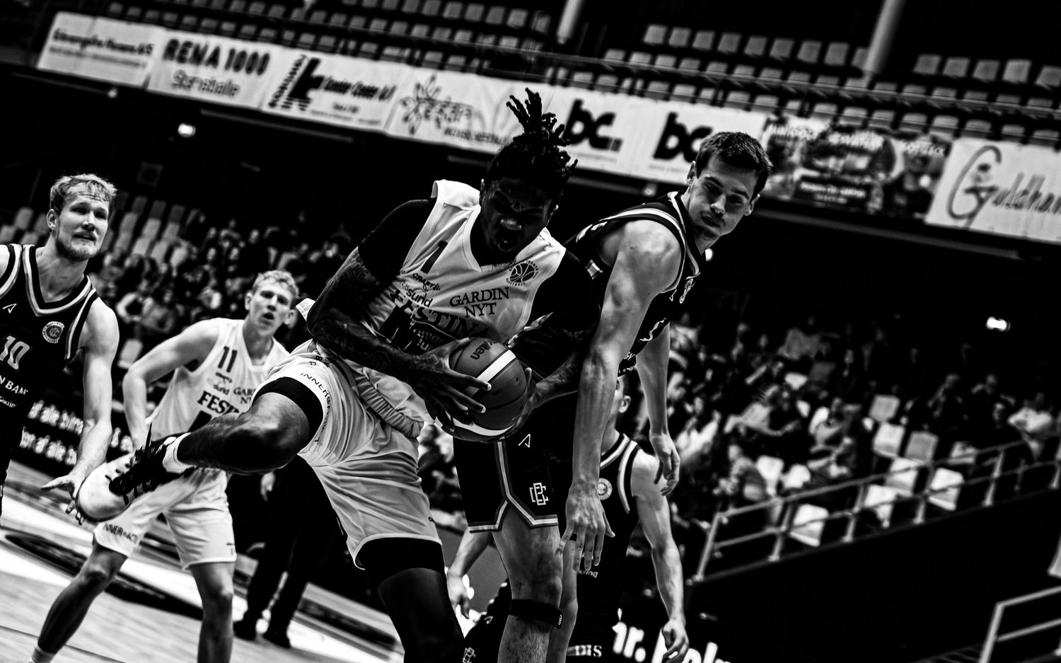 Black and white basketball game photo showing physical contact between players fighting for possession.