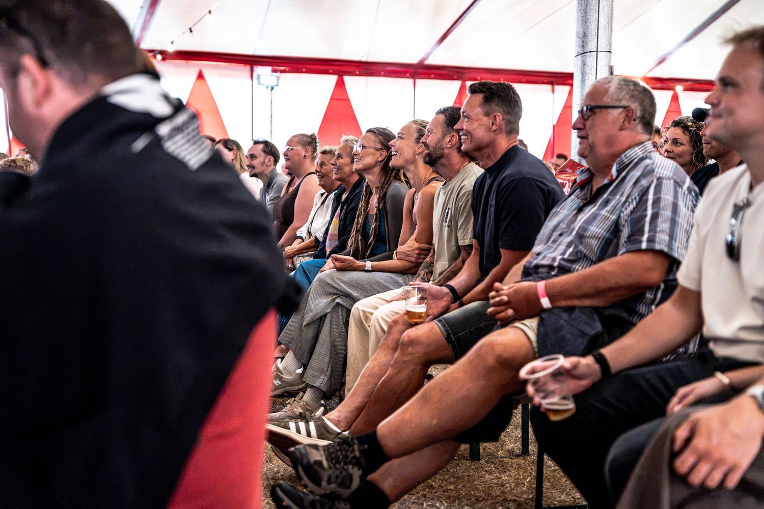 Audience seated in a red and white tent watching a live performance.