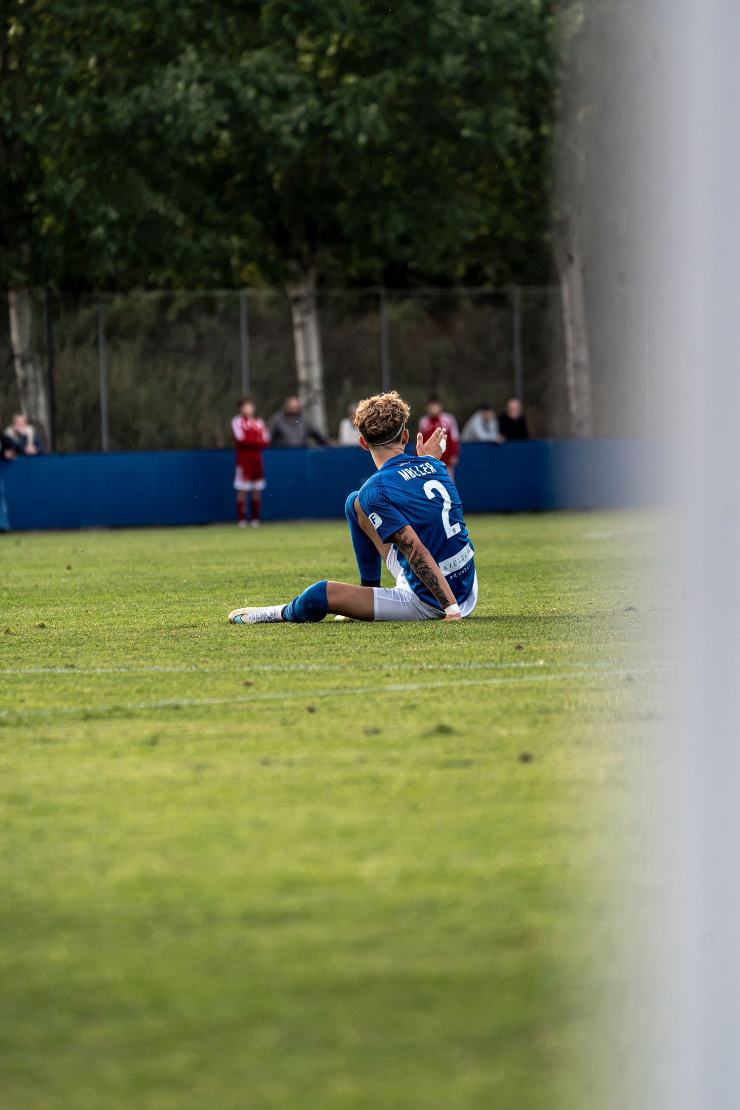 Soccer player number 2 sitting on the grass field during a match looking dejected.