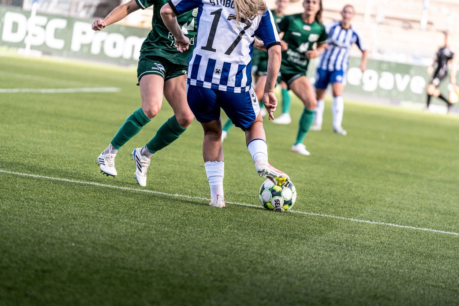 Close-up of female soccer players competing for ball control during a women's football match on turf.