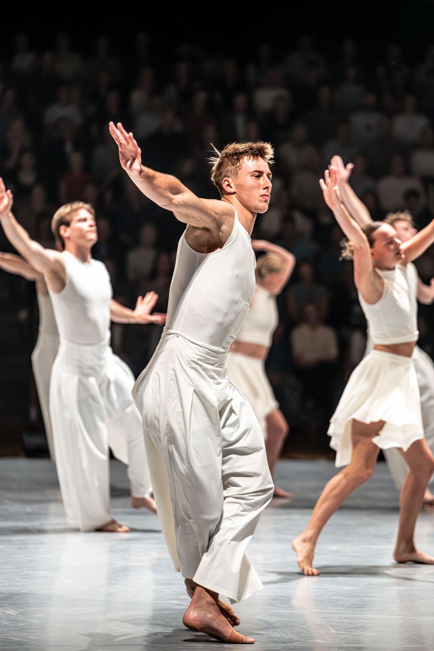 Male dancer in white sleeveless top and pants executes an expressive pose on stage.