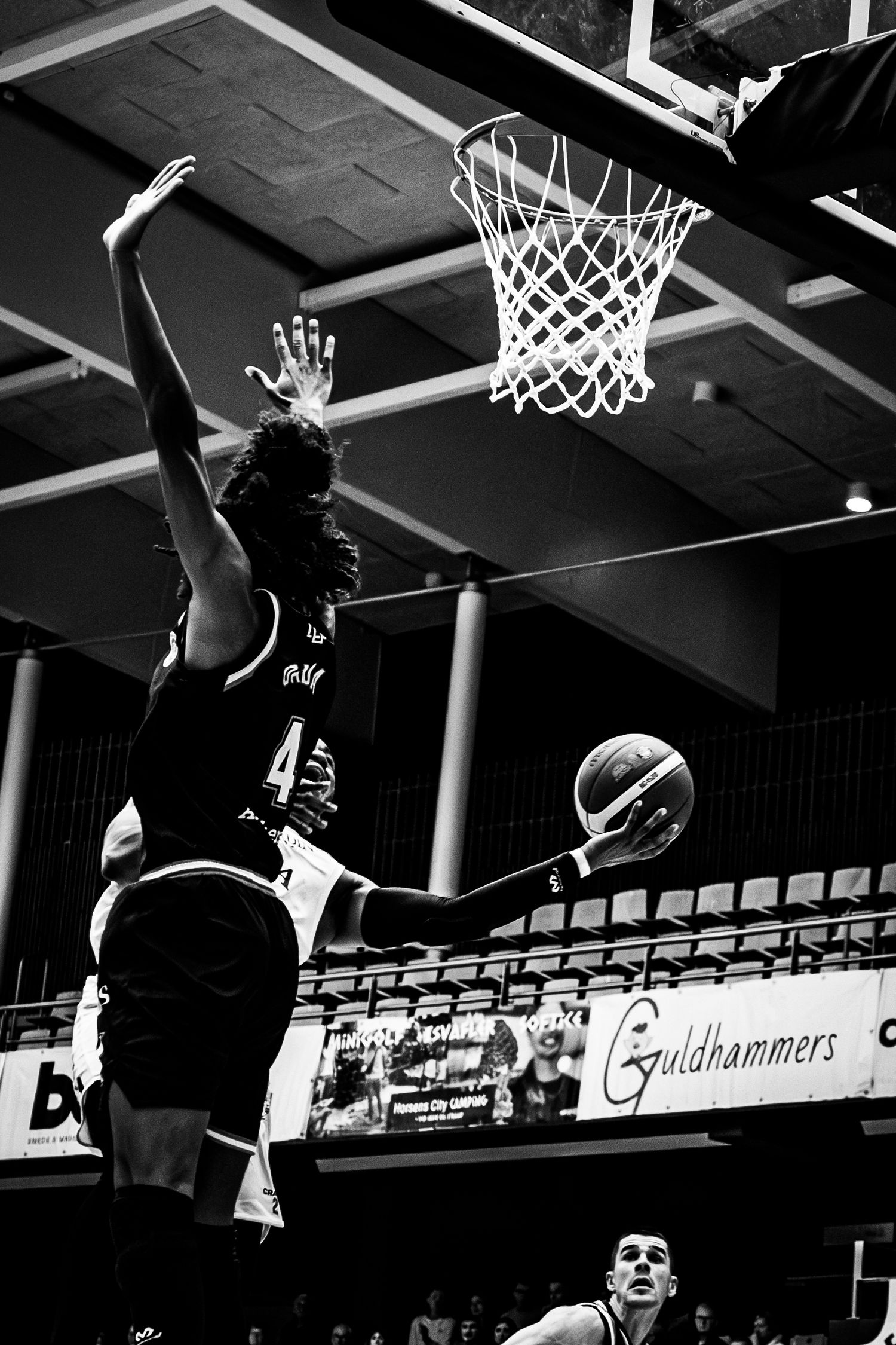 Black and white basketball photo of player attempting layup while defender reaches to block shot.