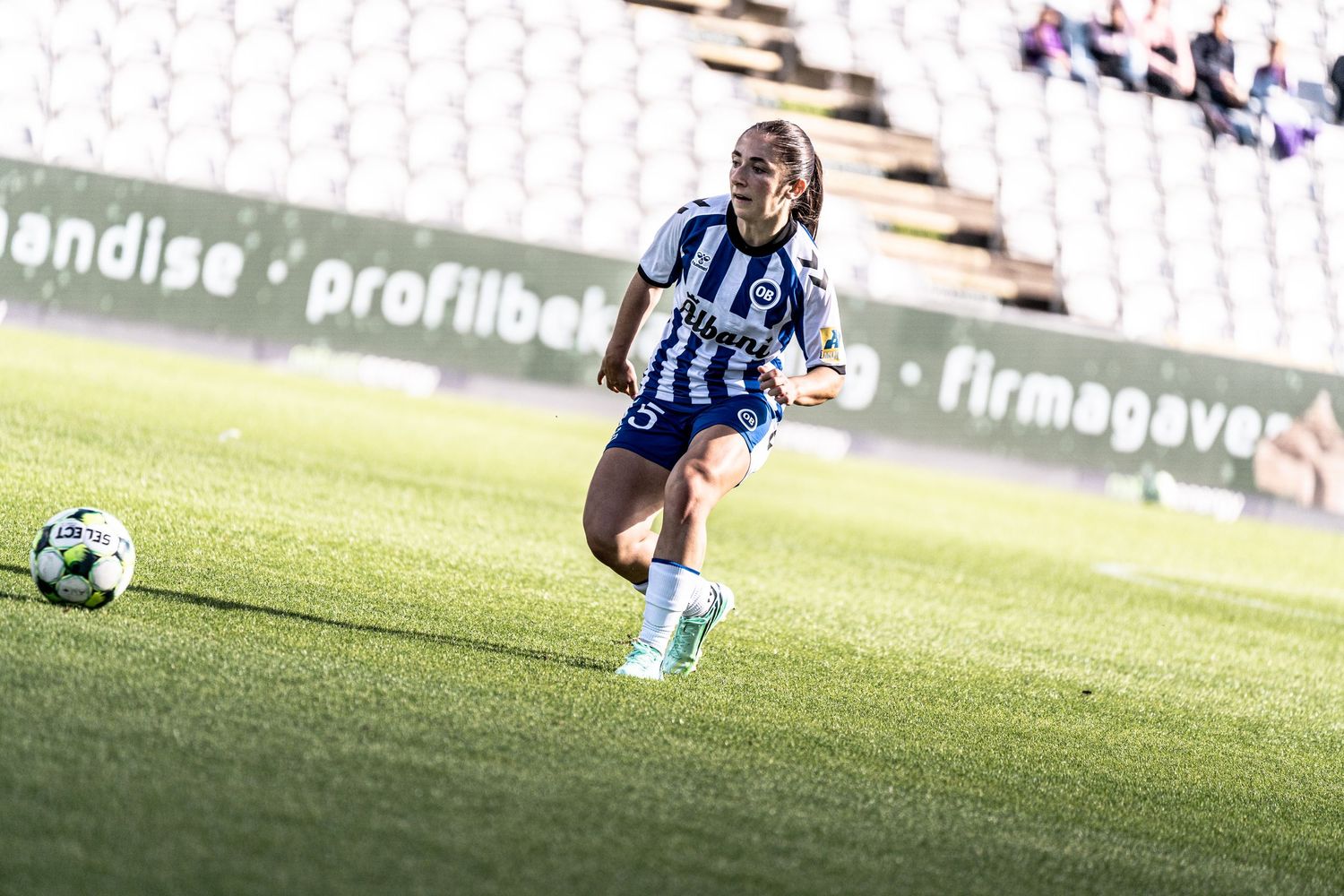 Female soccer player in blue-white kit dribbles ball across green pitch during a women's football match.