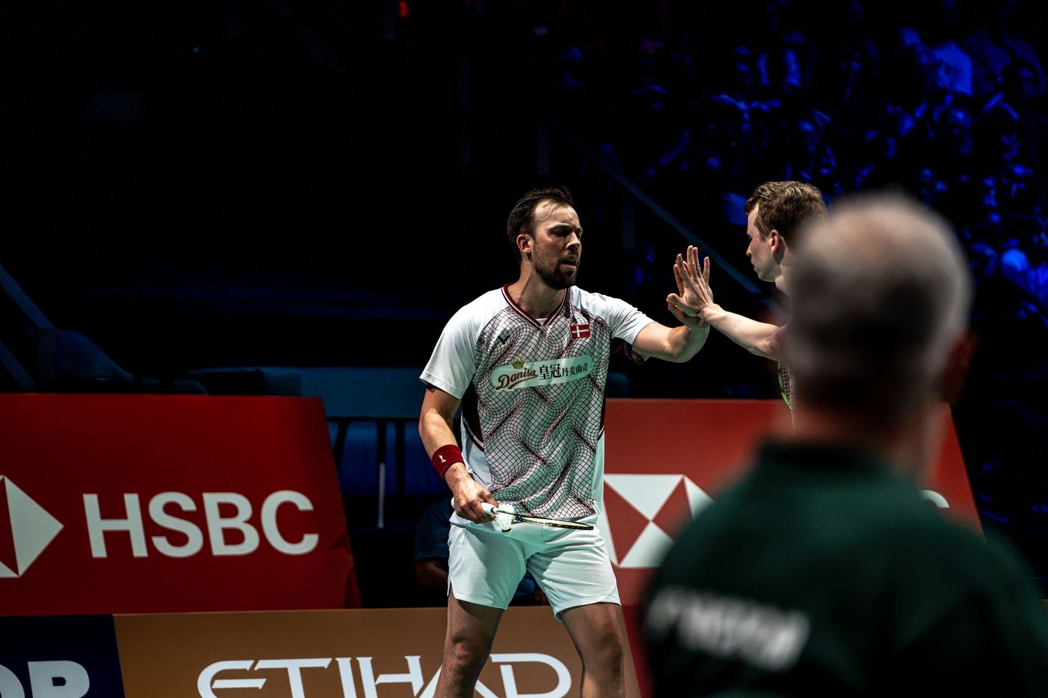 Two badminton doubles players celebrating with high-five on court at HSBC Etihad sponsored tournament.