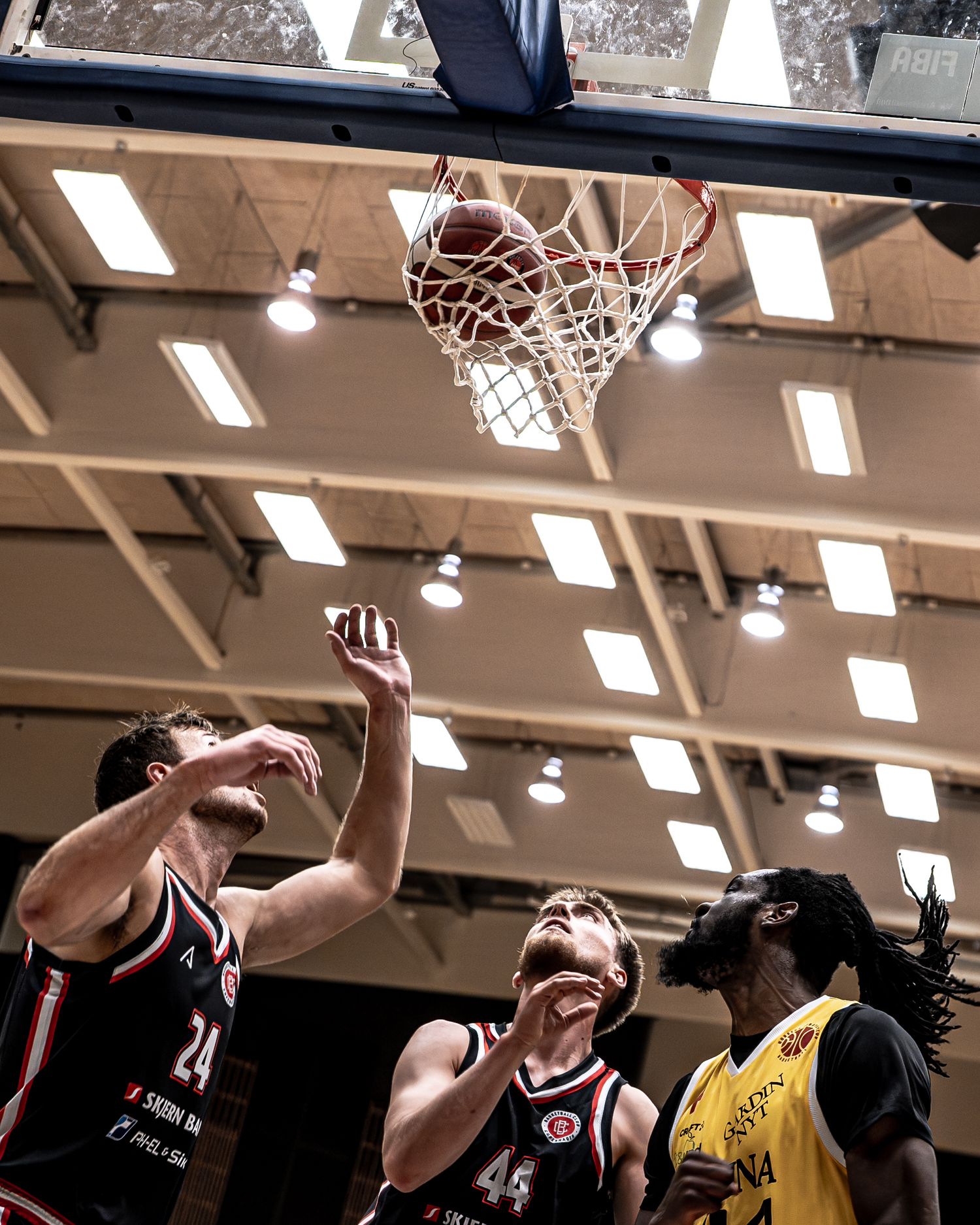 Two defenders in dark jerseys contest a shot attempt near the basket during basketball game.
