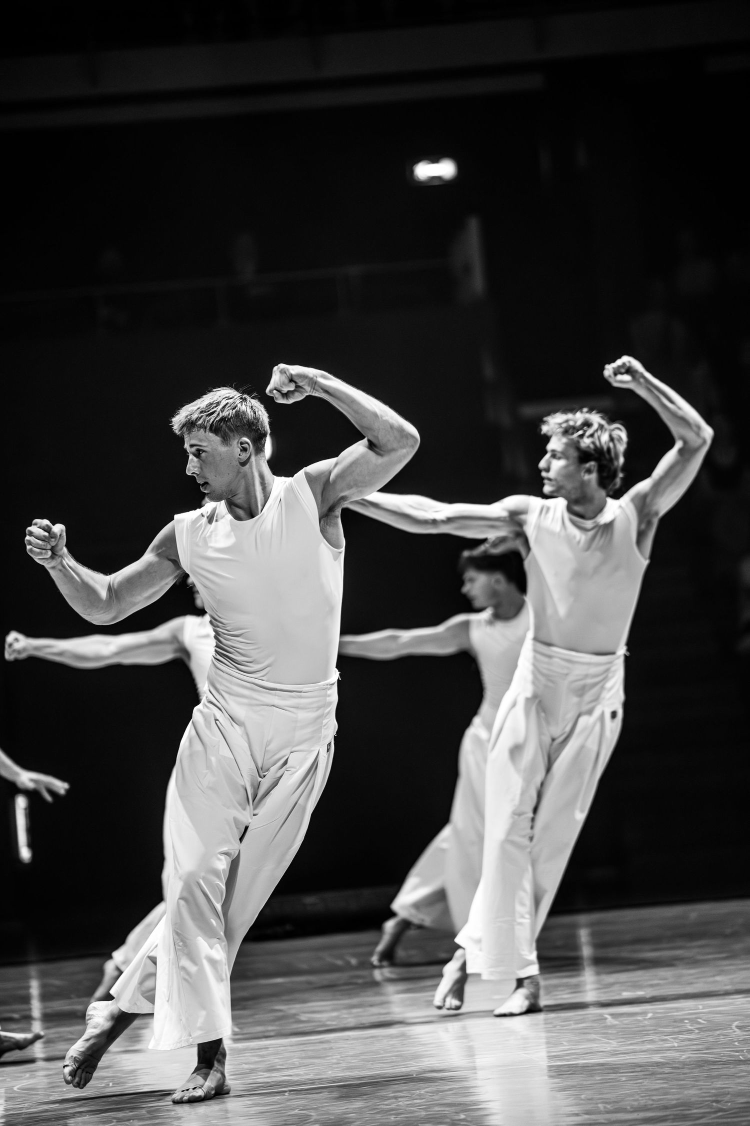 Two male dancers in white perform powerful choreography with raised fists in black and white.