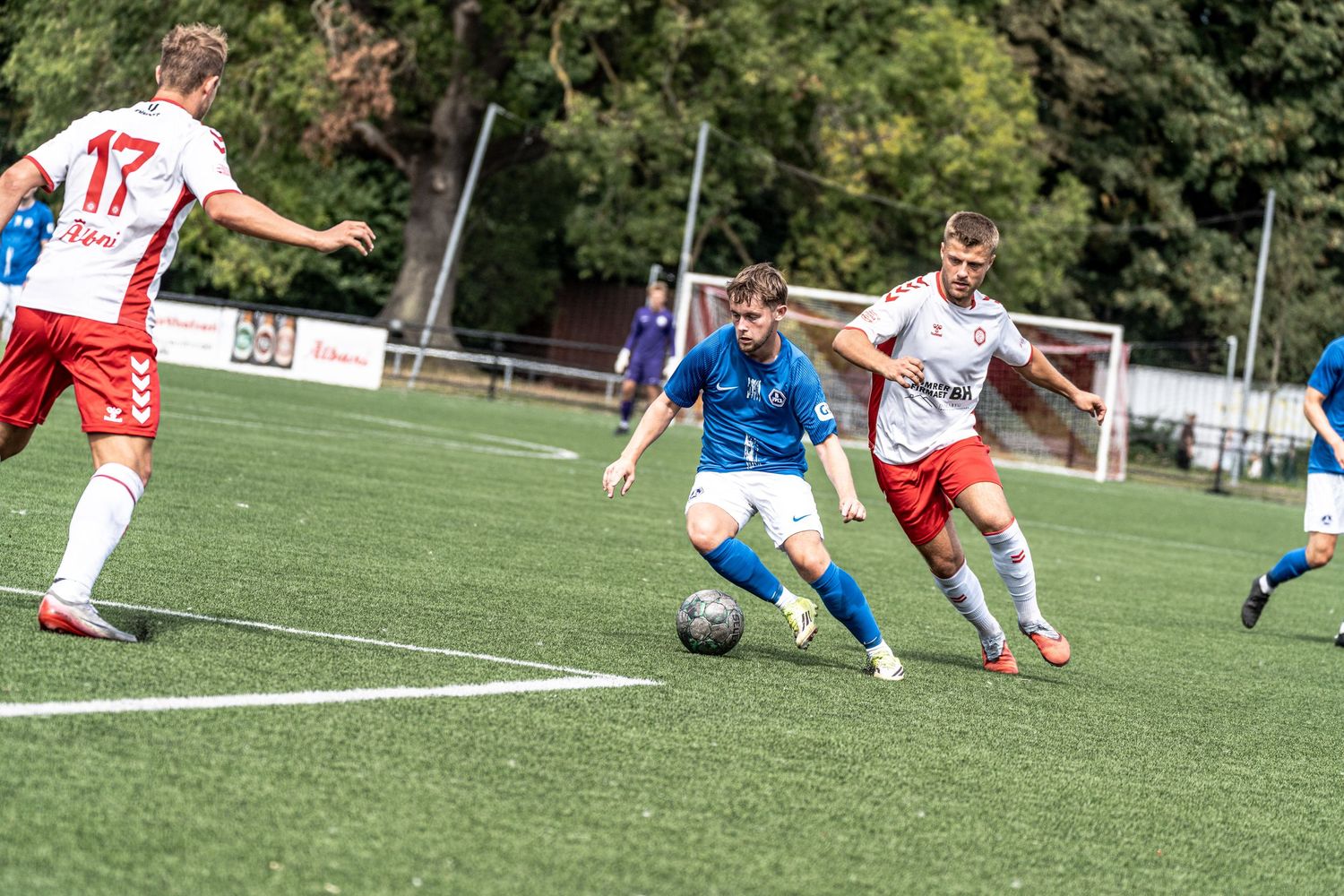 Soccer players in blue and red-white uniforms competing for the ball on a green field.