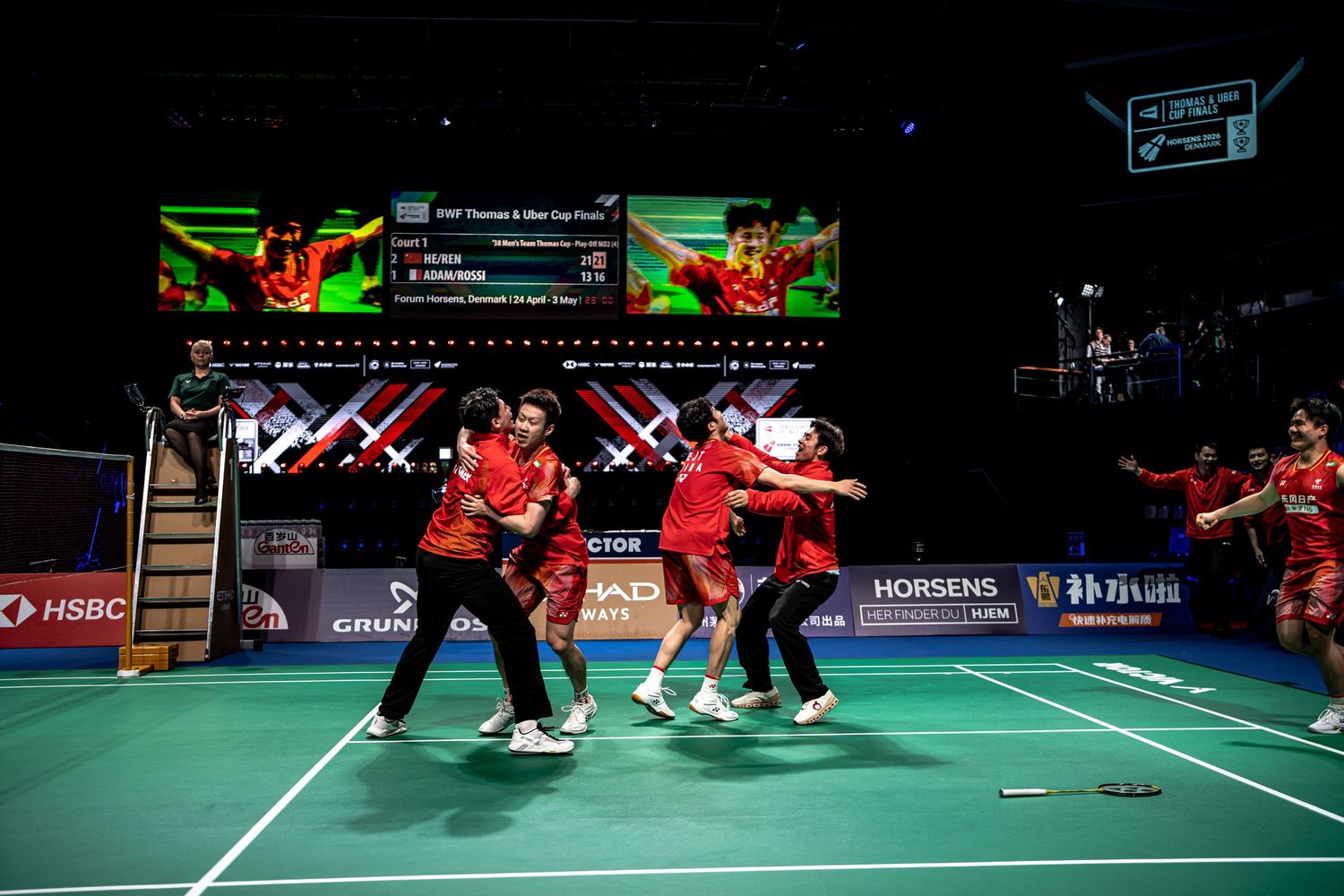 Chinese badminton team celebrating Thomas Cup Finals victory on court with team members rushing to join celebration.