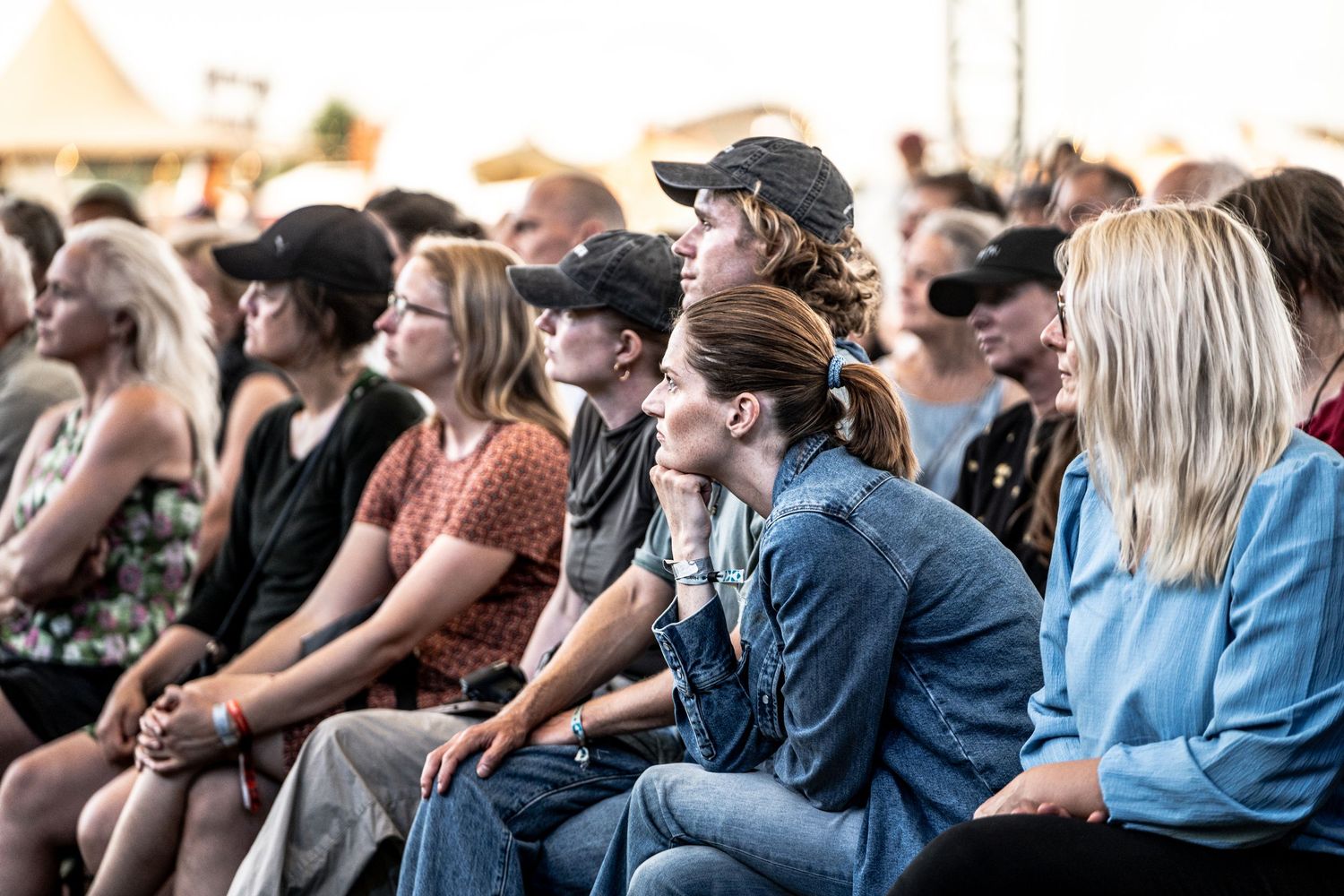 Engaged audience members sitting attentively at an outdoor festival event on a sunny day.
