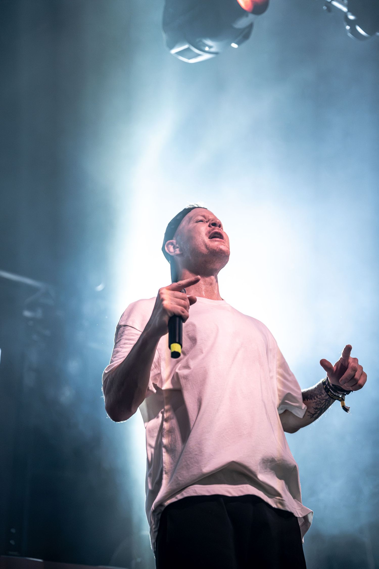 Male singer in white t-shirt performs with microphone under blue stage lights.