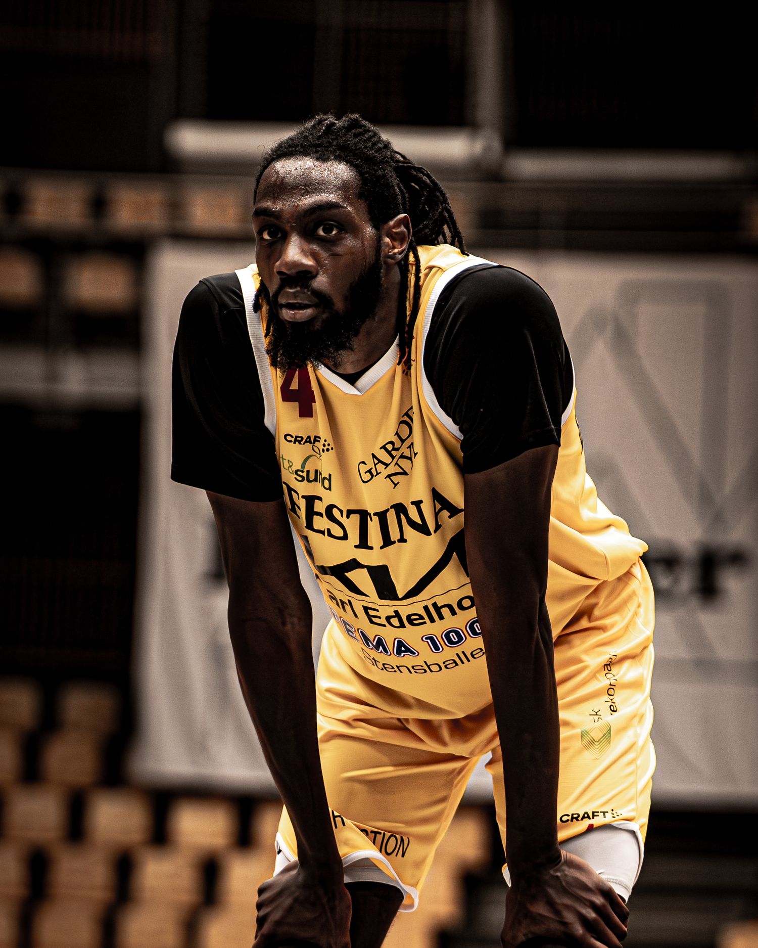 Focused professional basketball player wearing yellow number 4 jersey rests during a timeout in an indoor arena.