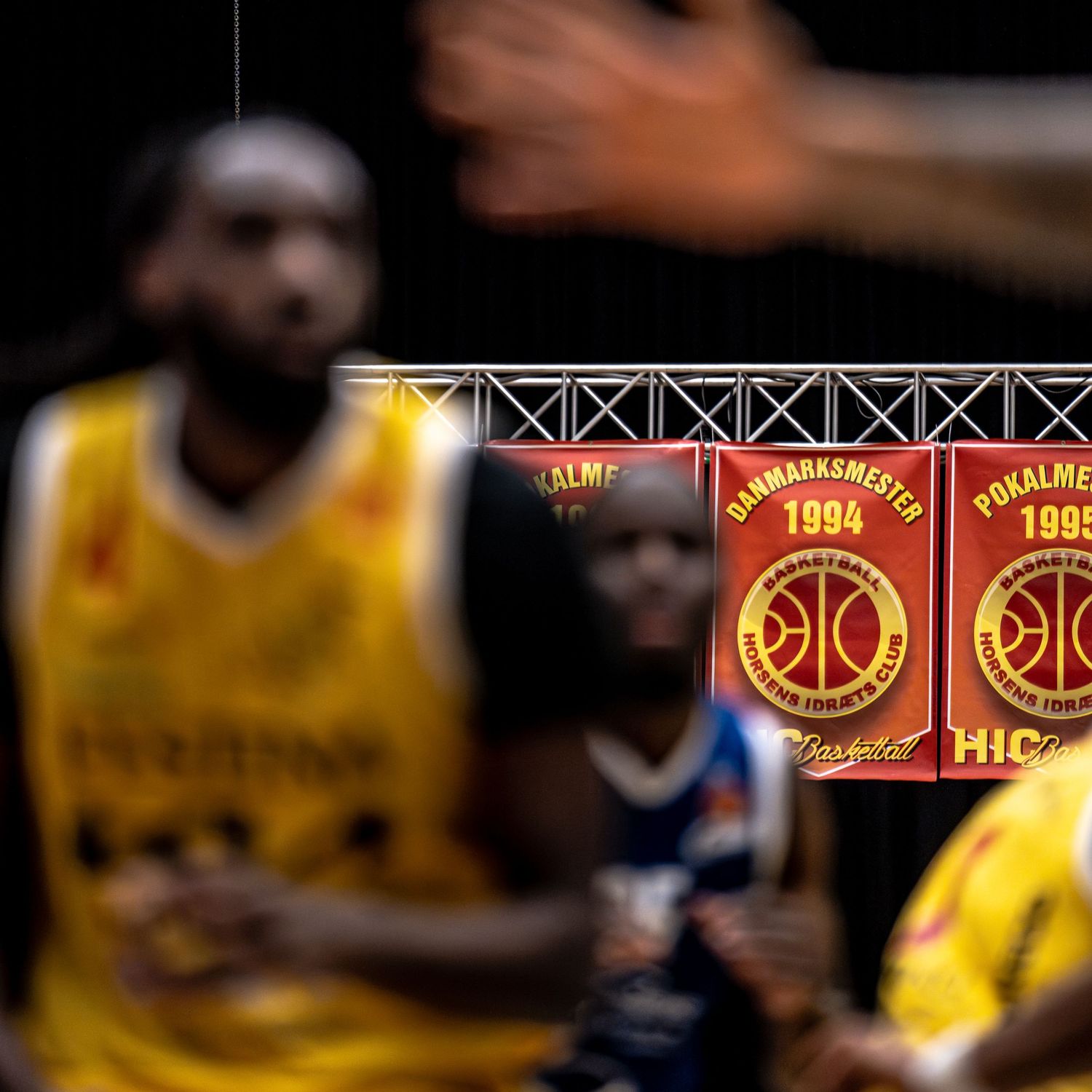 Danish basketball championship banners from 1994 and 1995 displayed at a professional basketball game arena.