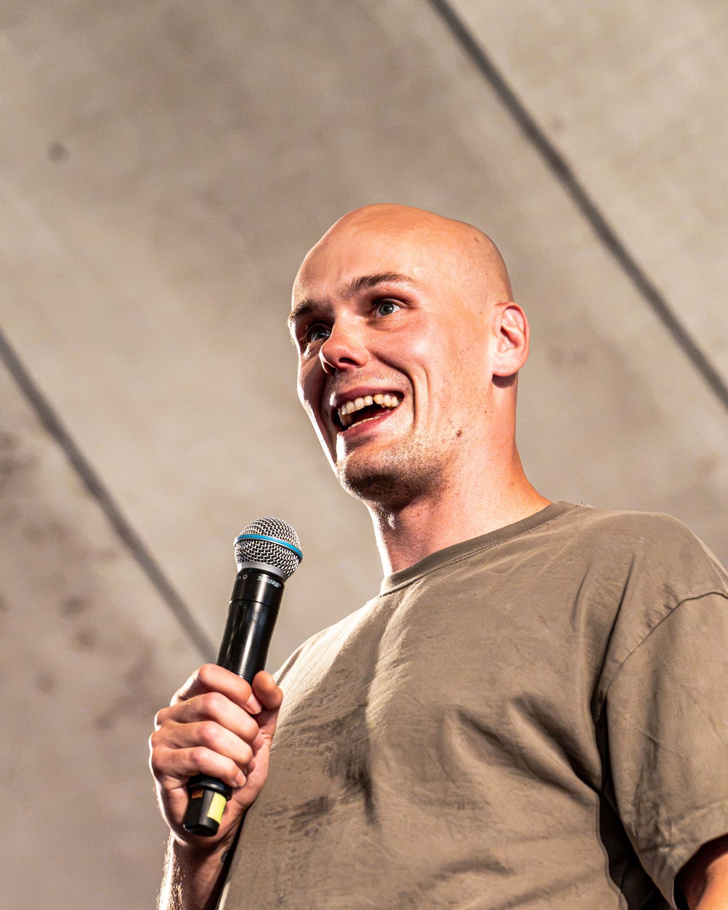 Bald man smiling and holding a microphone while performing on stage.