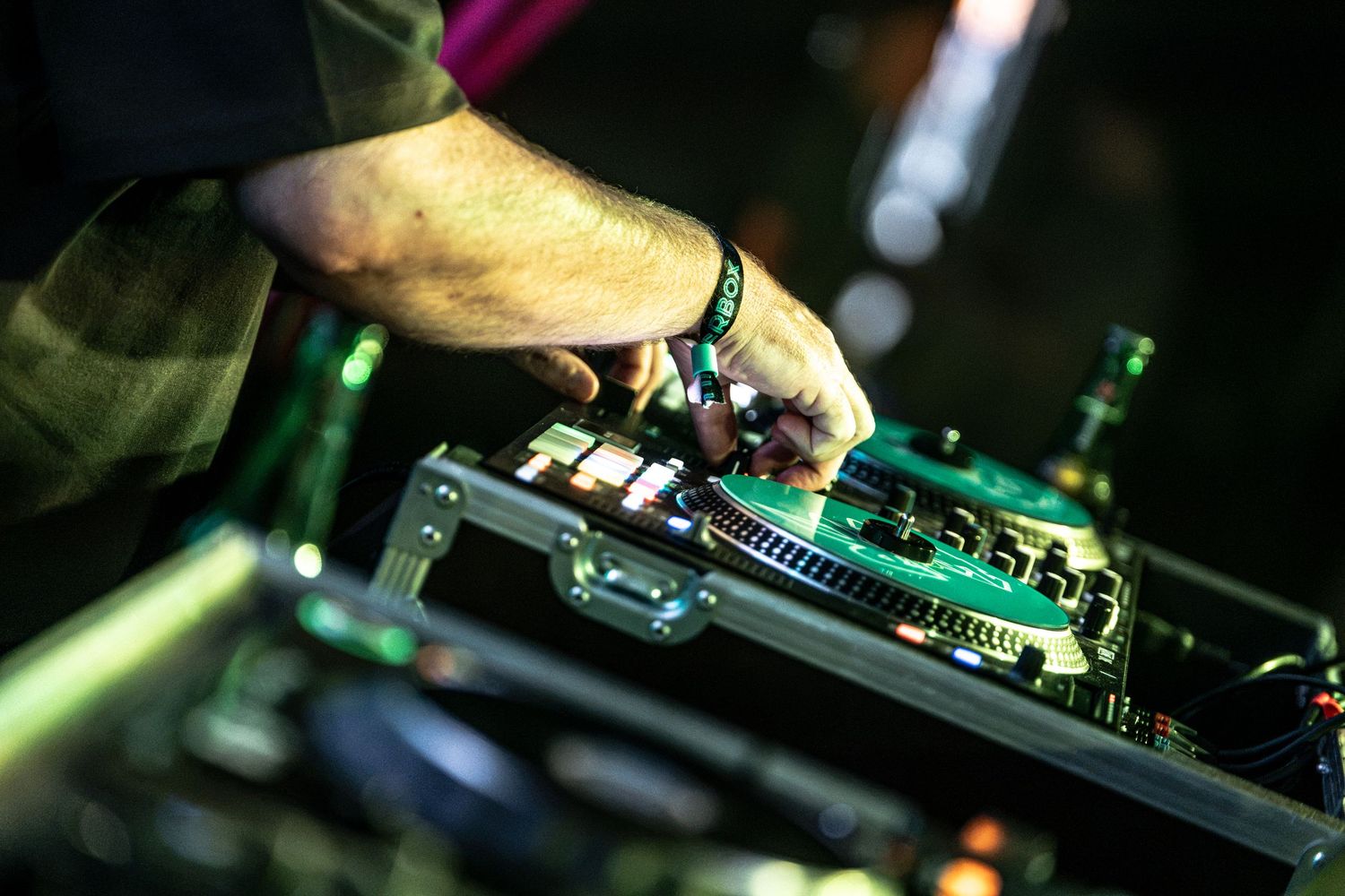 Close-up of DJ hands mixing on turntables with green lighting at live music event.