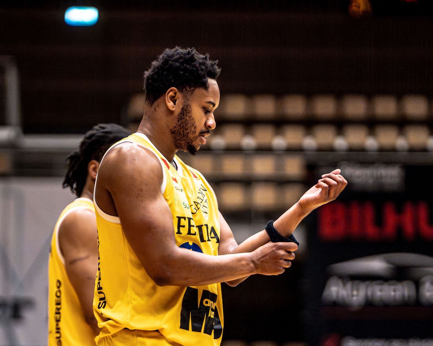 Yellow-uniformed basketball player adjusts wristband during a professional basketball league game.