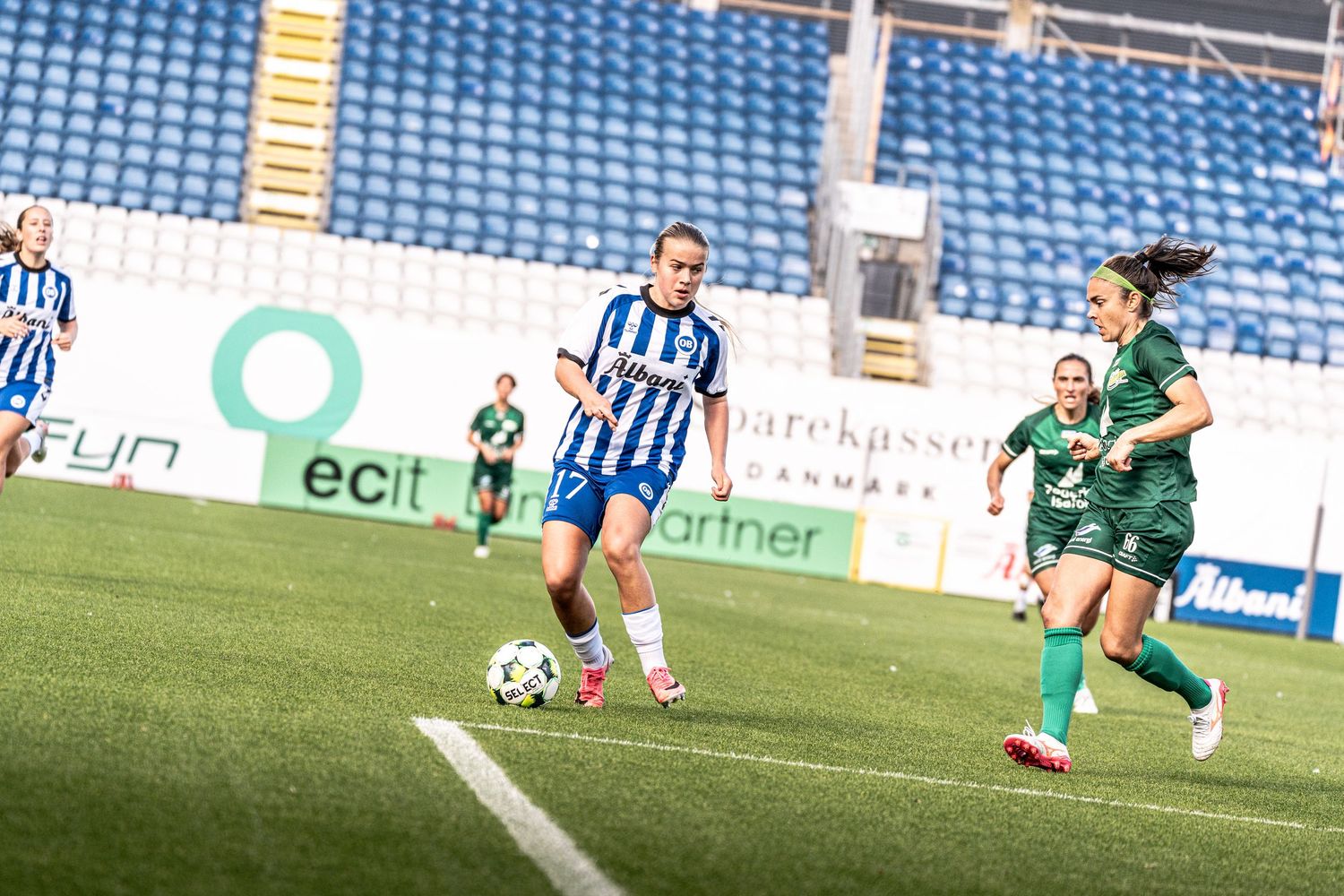Female soccer player in blue and white kit dribbles ball during a women's football match on green pitch.