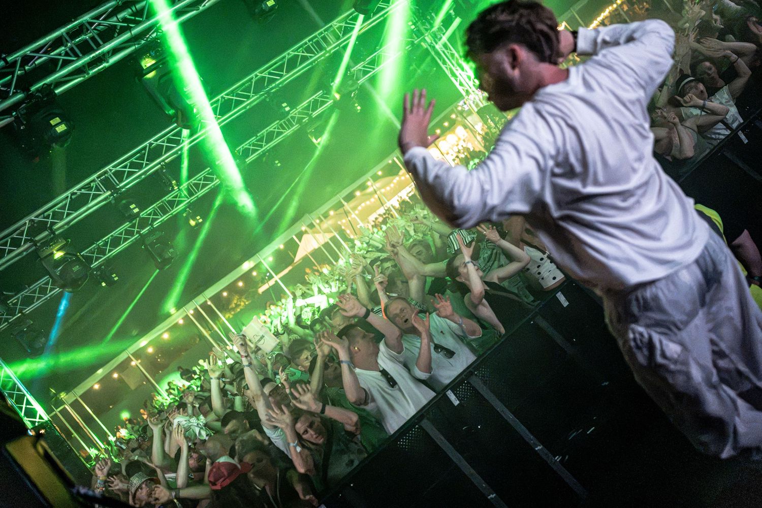 Energetic performer stage dives into crowd under green laser lights at live concert.