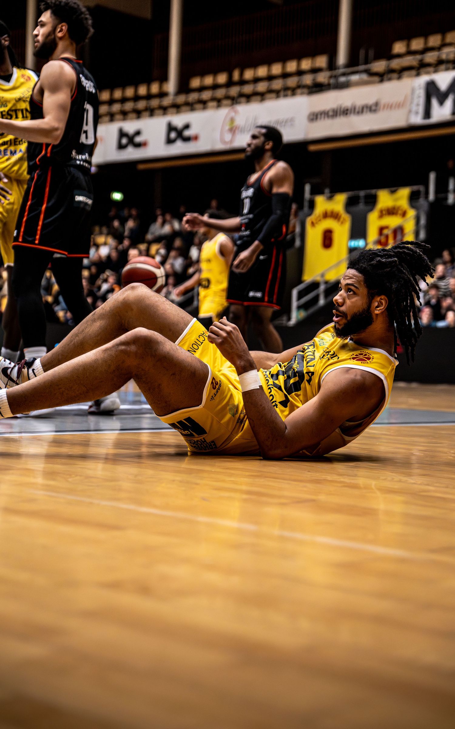 Basketball player in yellow uniform sits on court floor during a professional league game.