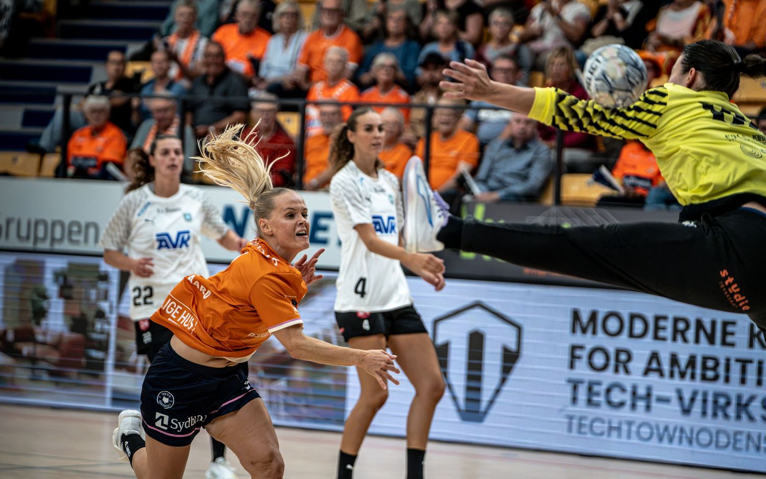 Female handball player leaps to shoot at goal during an intense indoor women's handball match.