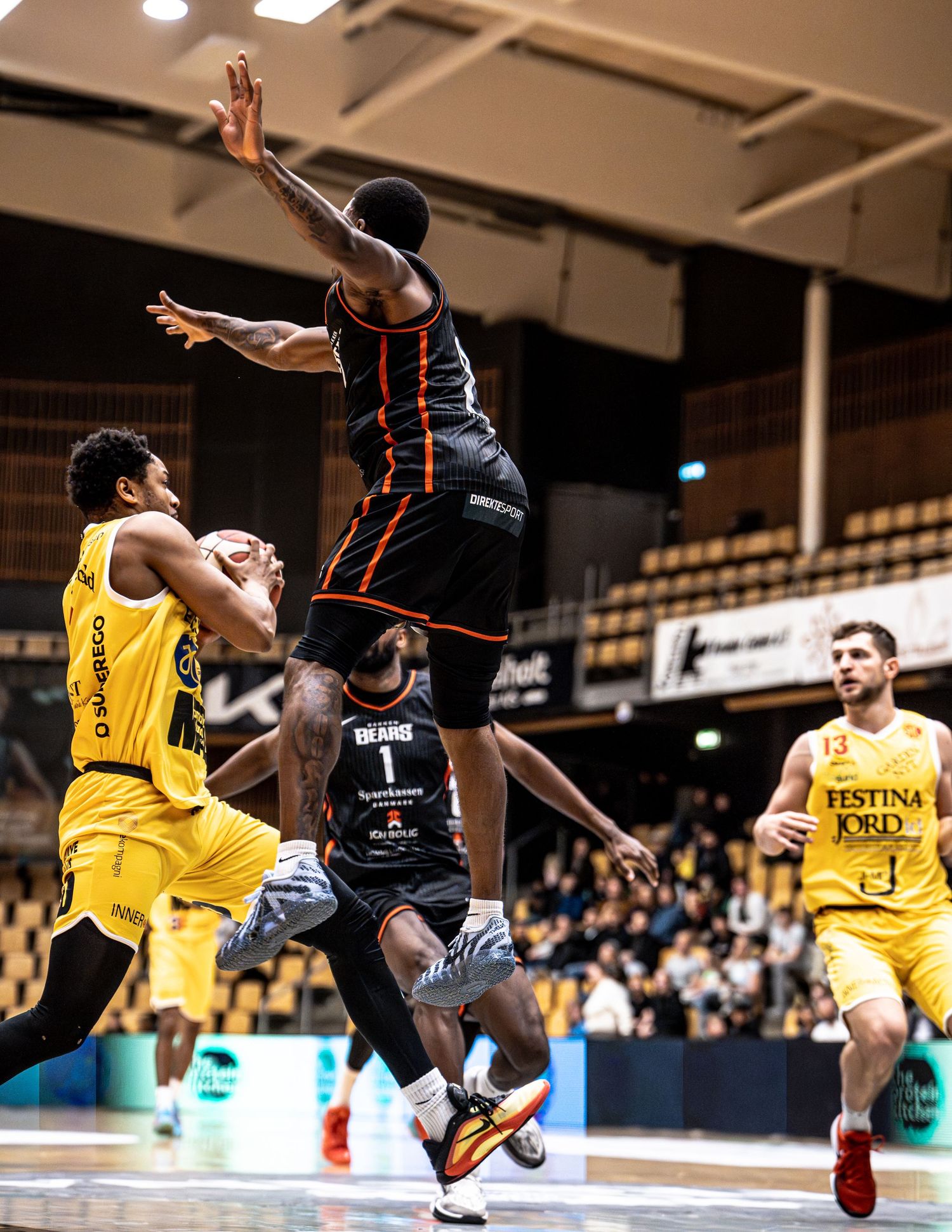 Black-uniformed player leaps to block a shot during an intense basketball game.