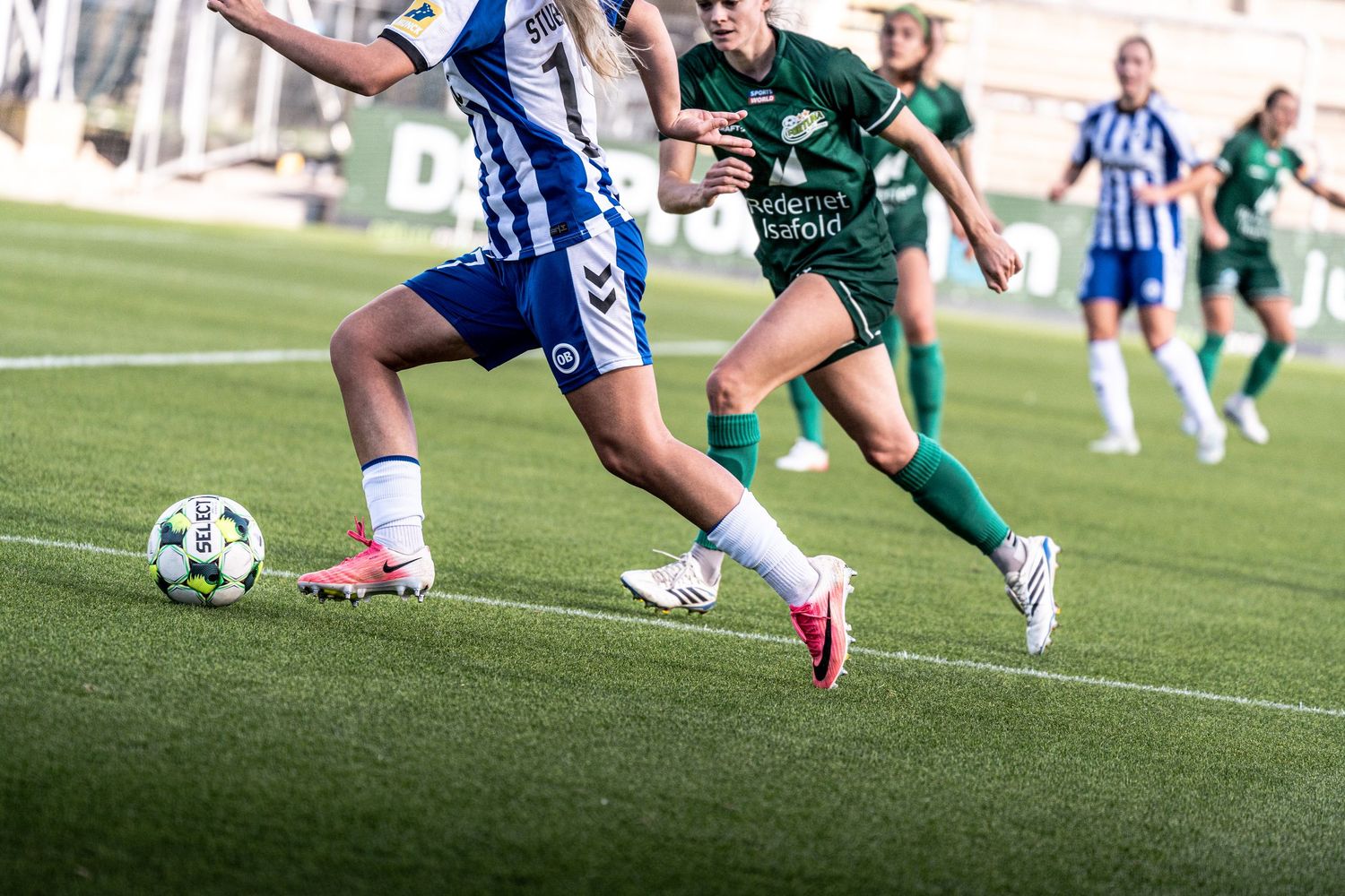 Women's soccer players in green uniforms surround a blue and white kitted player controlling the ball.
