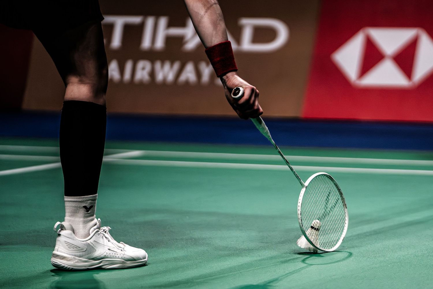 Close-up of badminton player holding racket near shuttlecock on green court during a professional match.